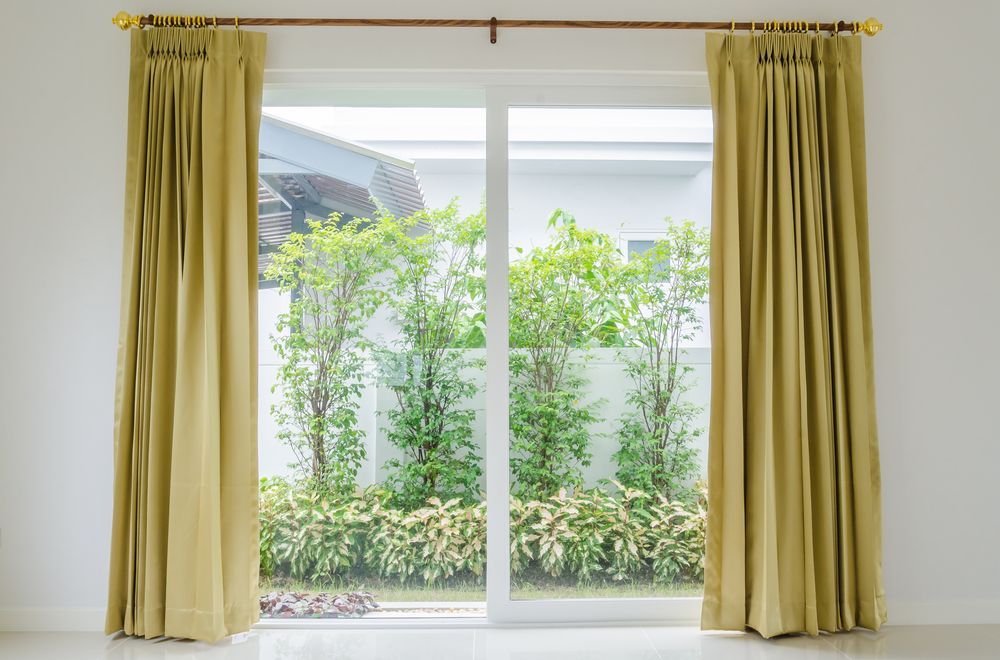A Sliding Glass Door With Yellow Curtain Opens — Window Coverings in Cardiff, NSW