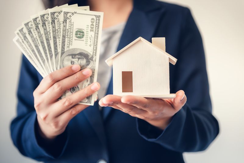A woman is holding a model house and a bunch of money.