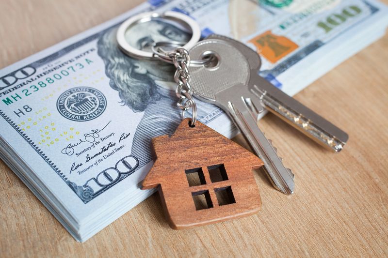 A house keychain is sitting on top of a stack of money.