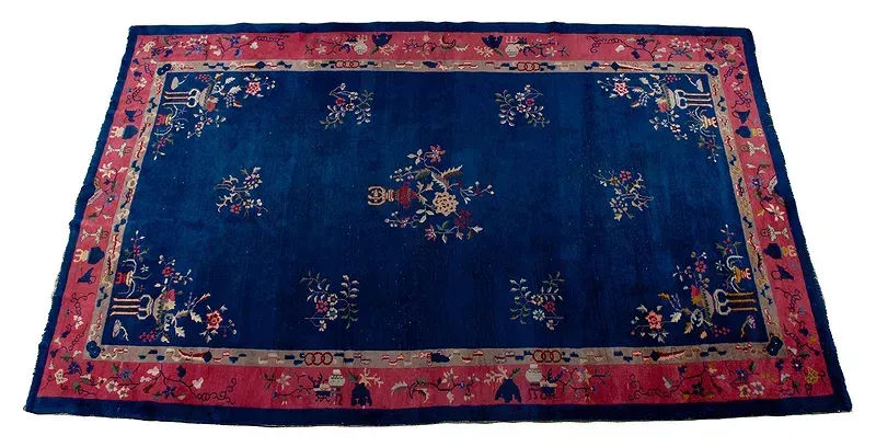 A blue rug with a red border and flowers on it