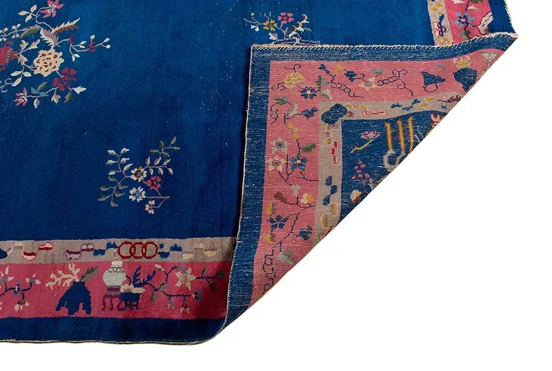 A blue rug with a pink border and flowers on it