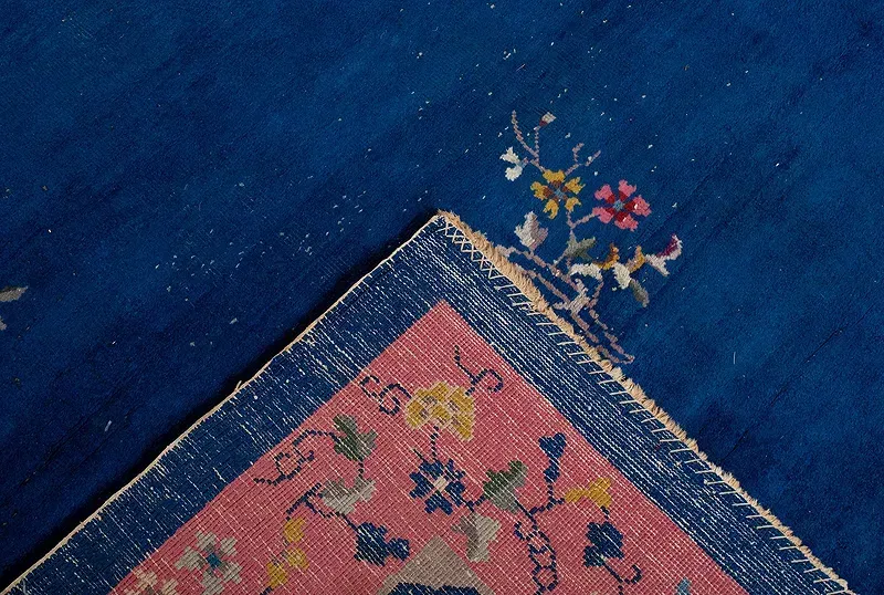 A blue rug with a pink border and flowers on it