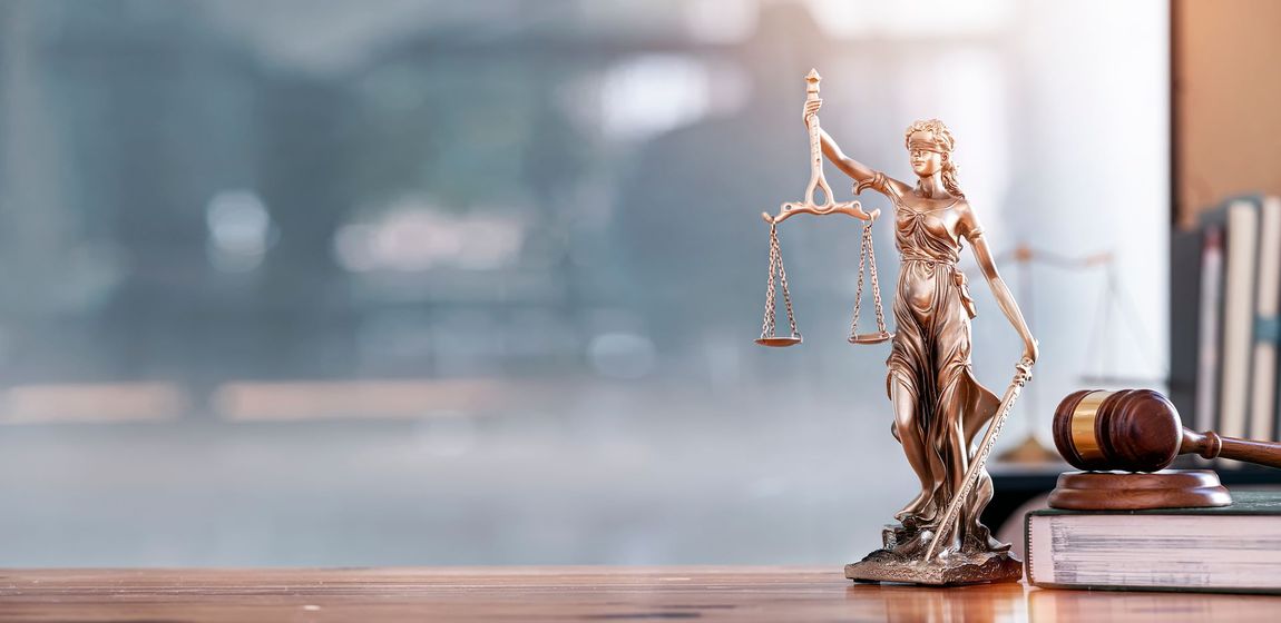 A statue of justice is sitting on a wooden table next to a gavel.