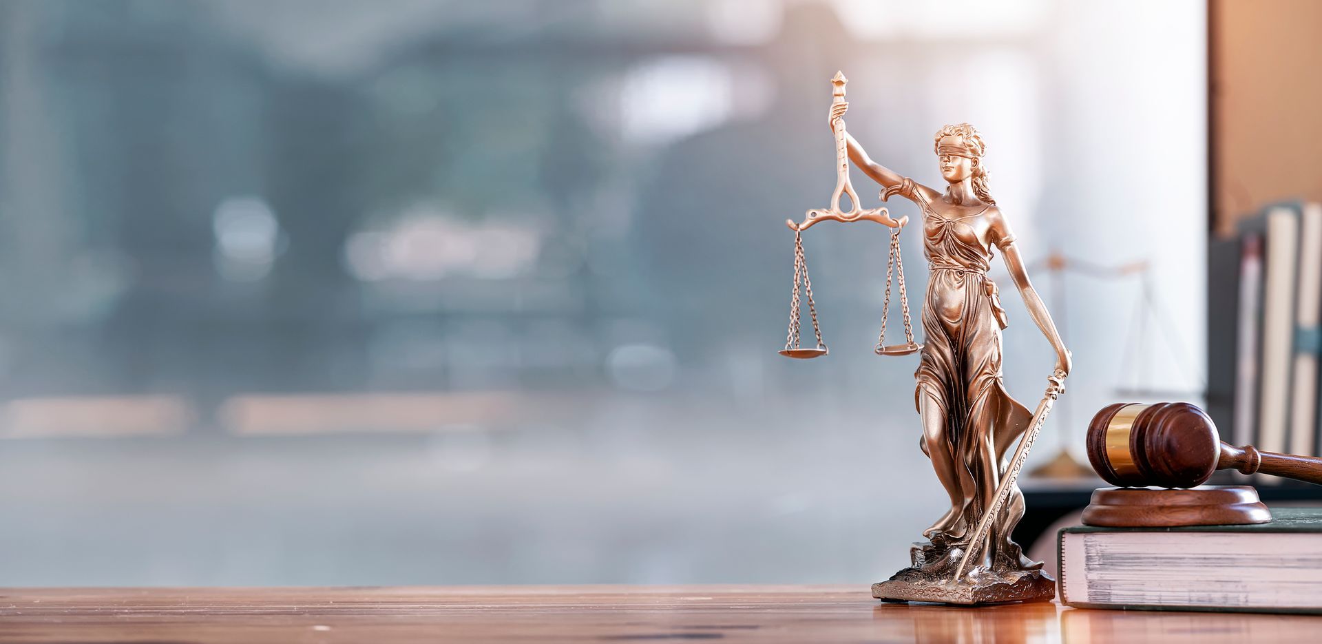 A statue of justice is sitting on a wooden table next to a gavel.
