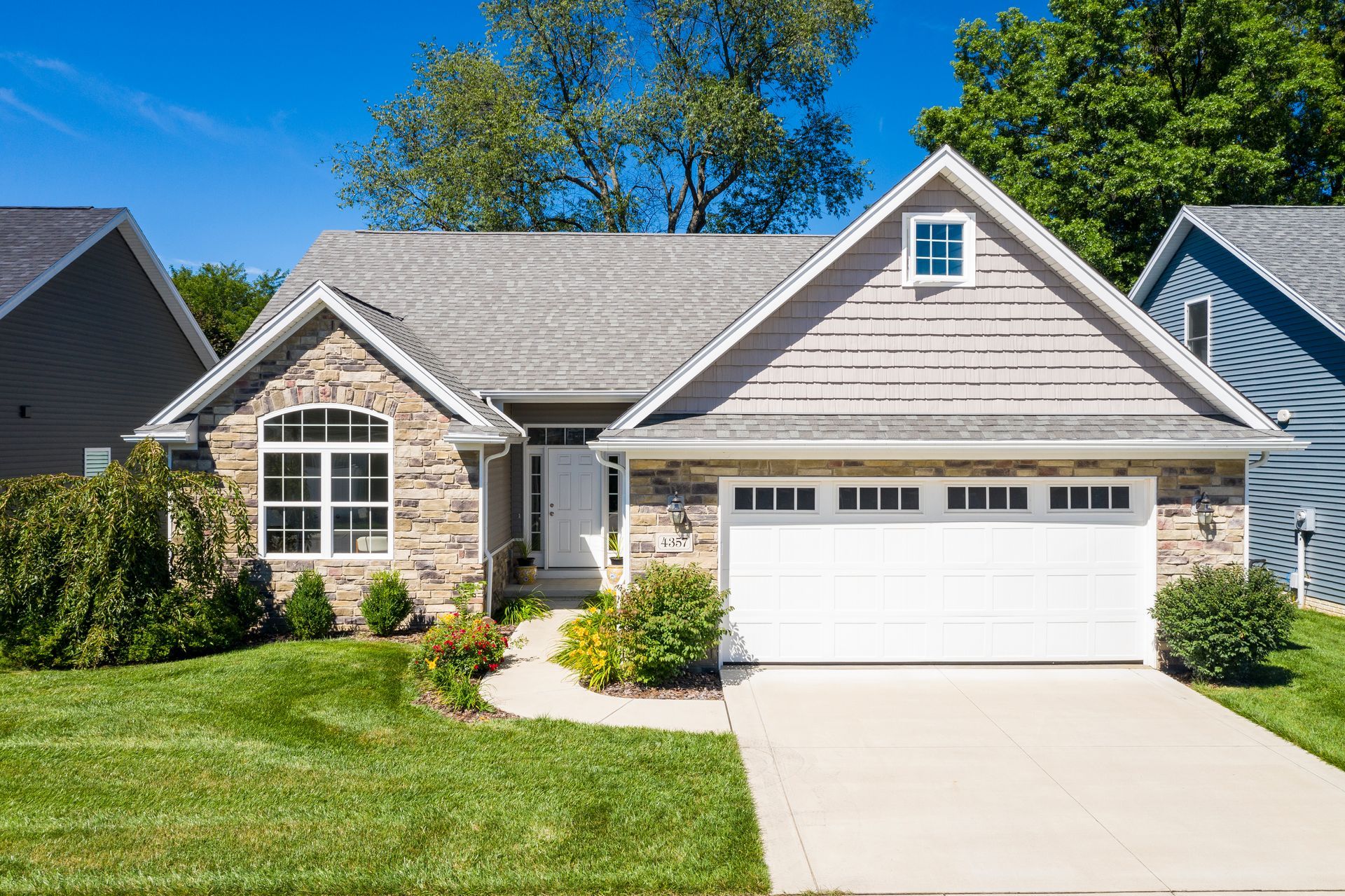 Stone and siding ranch house with attached garage, lush green lawn, blue sky.