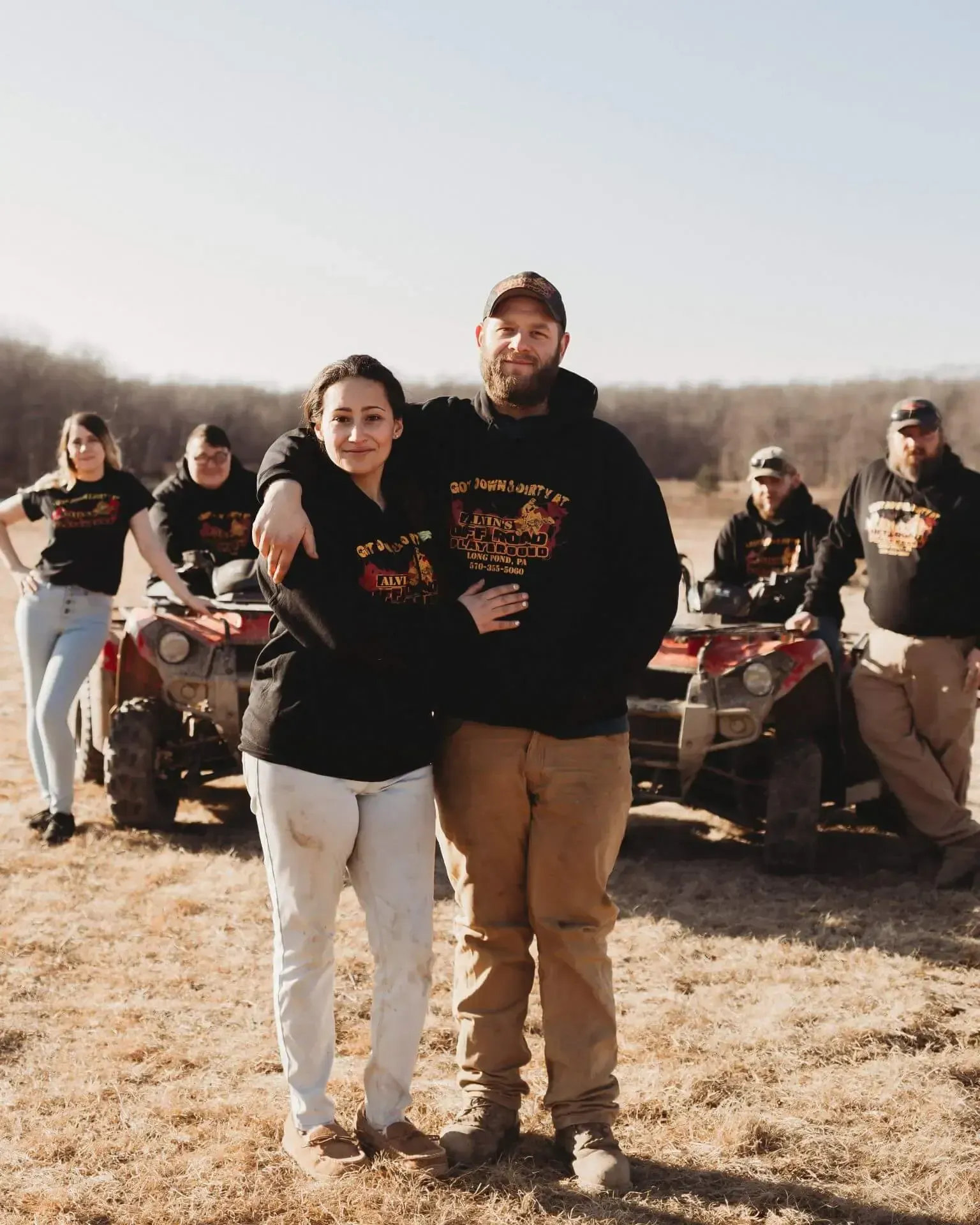 A man and a woman are posing for a picture in front of atvs.