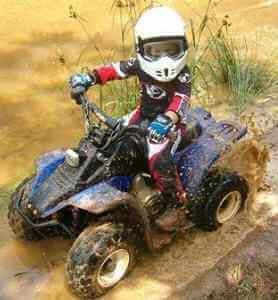 A young boy is riding a four wheeler through the mud.