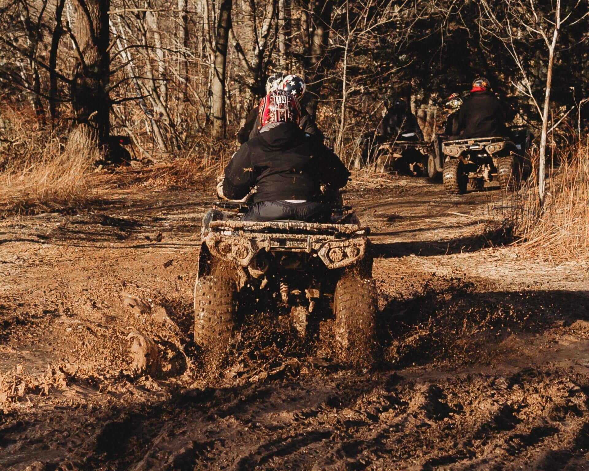A group of people are riding atvs down a muddy trail.