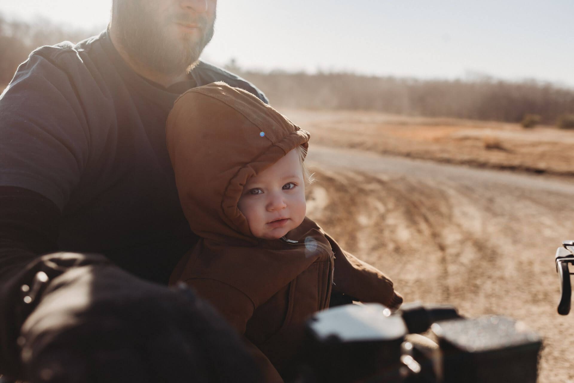 A man is holding a baby in his arms while riding a motorcycle.