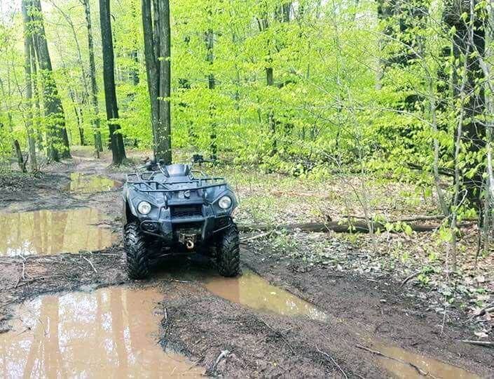 An atv is driving down a muddy road in the woods.