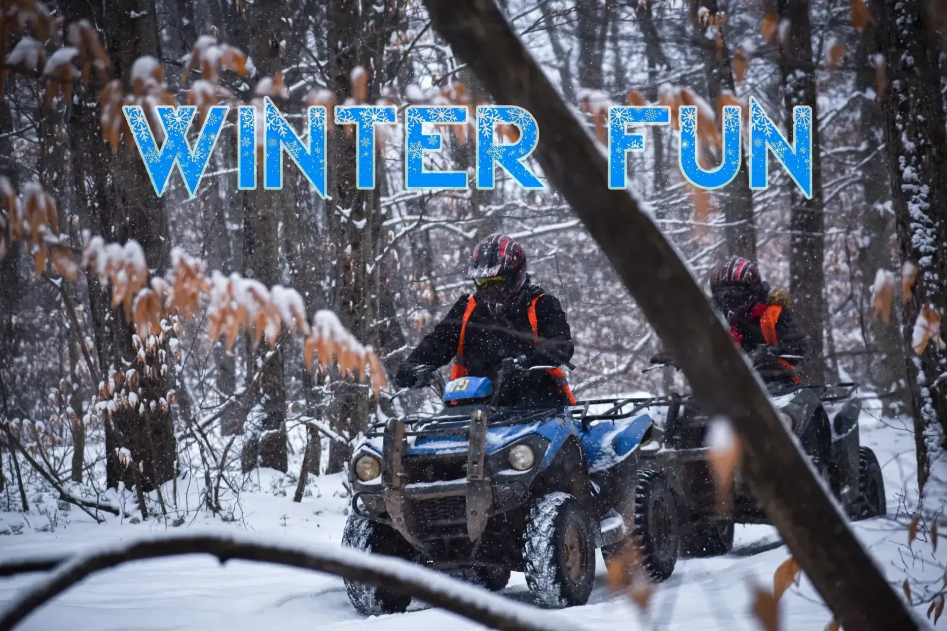 Two people are riding atvs in the snow in the woods.