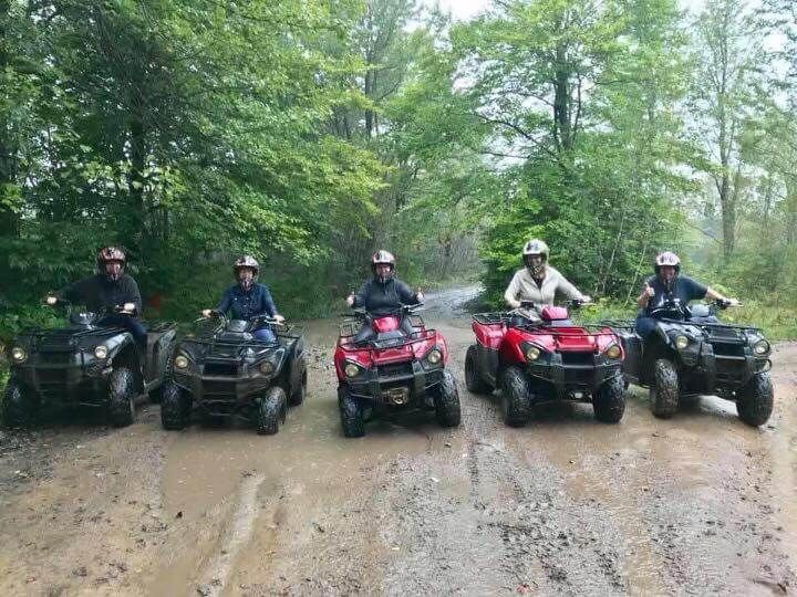 A group of people are riding atvs on a muddy road.