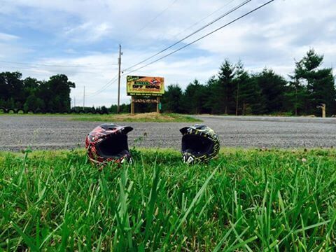 Two motorcycle helmets are laying in the grass near a road.