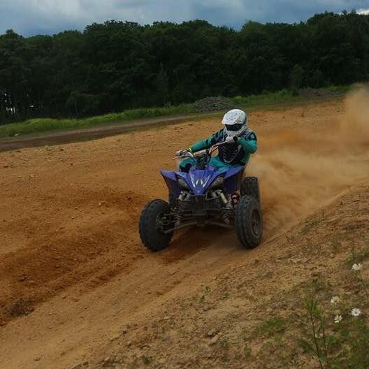 A man is riding a blue atv on a dirt road