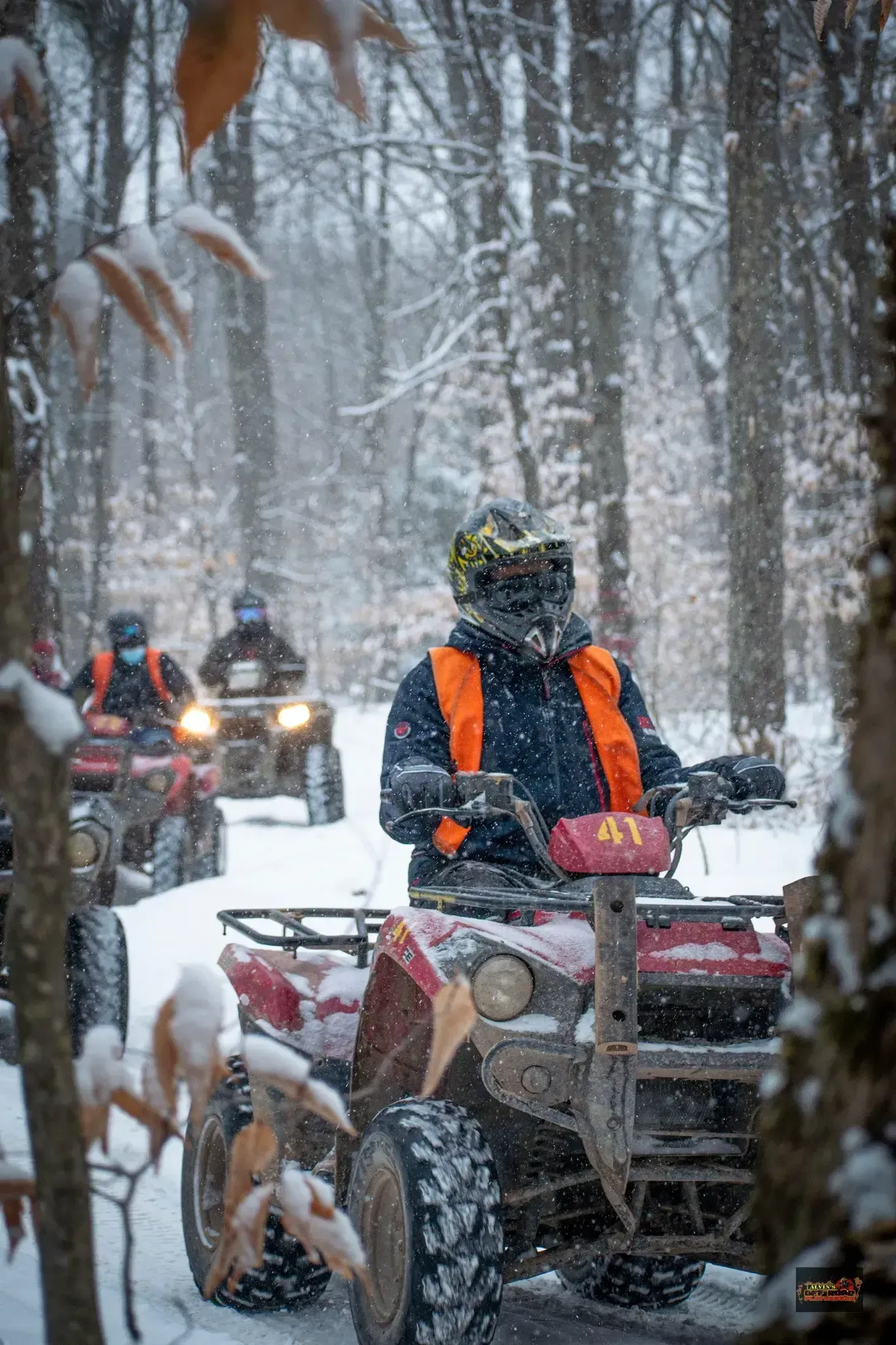 A group of people are riding atvs in the snow in the woods.