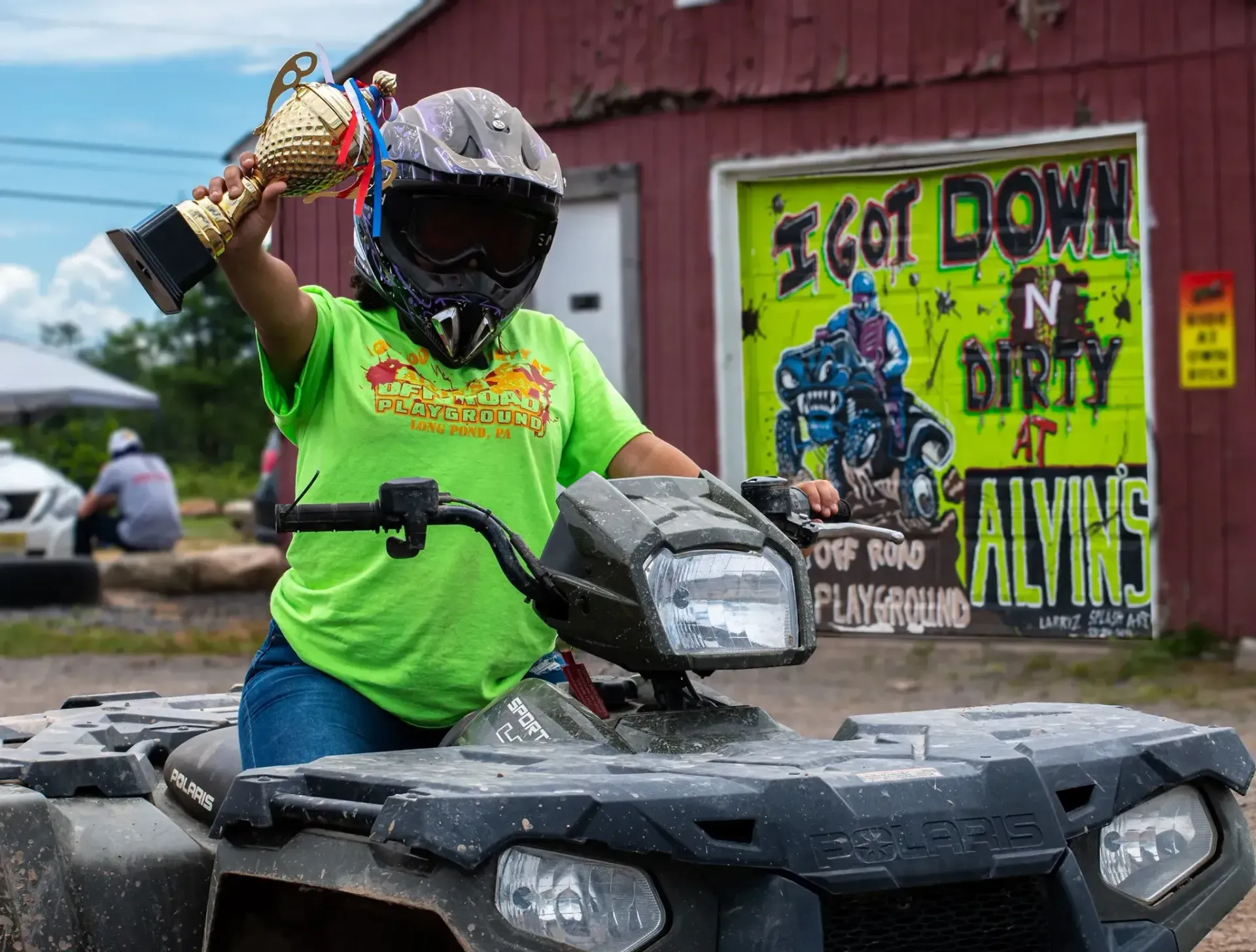 A person is riding an atv and holding a trophy.