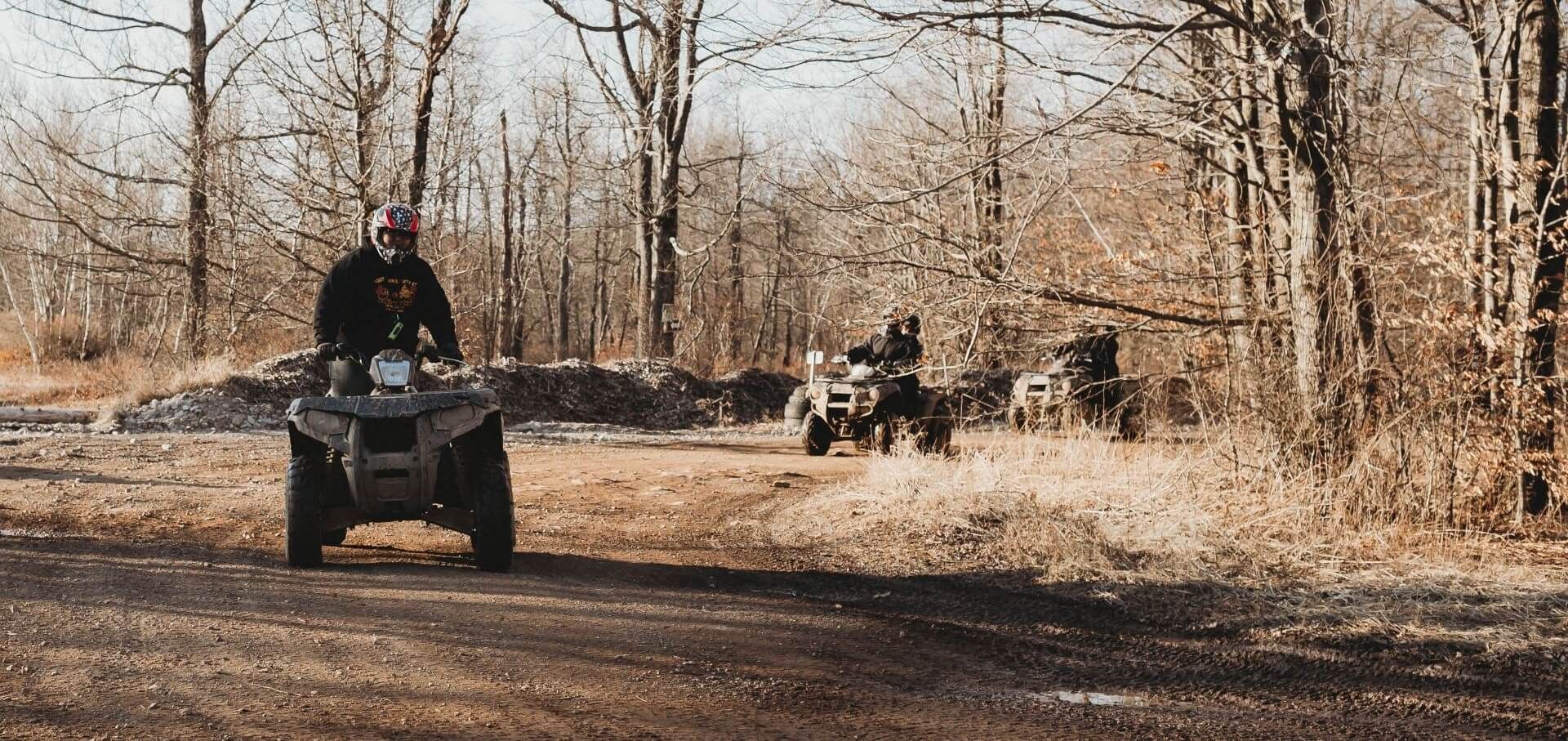 A man is riding an atv down a dirt road in the woods.