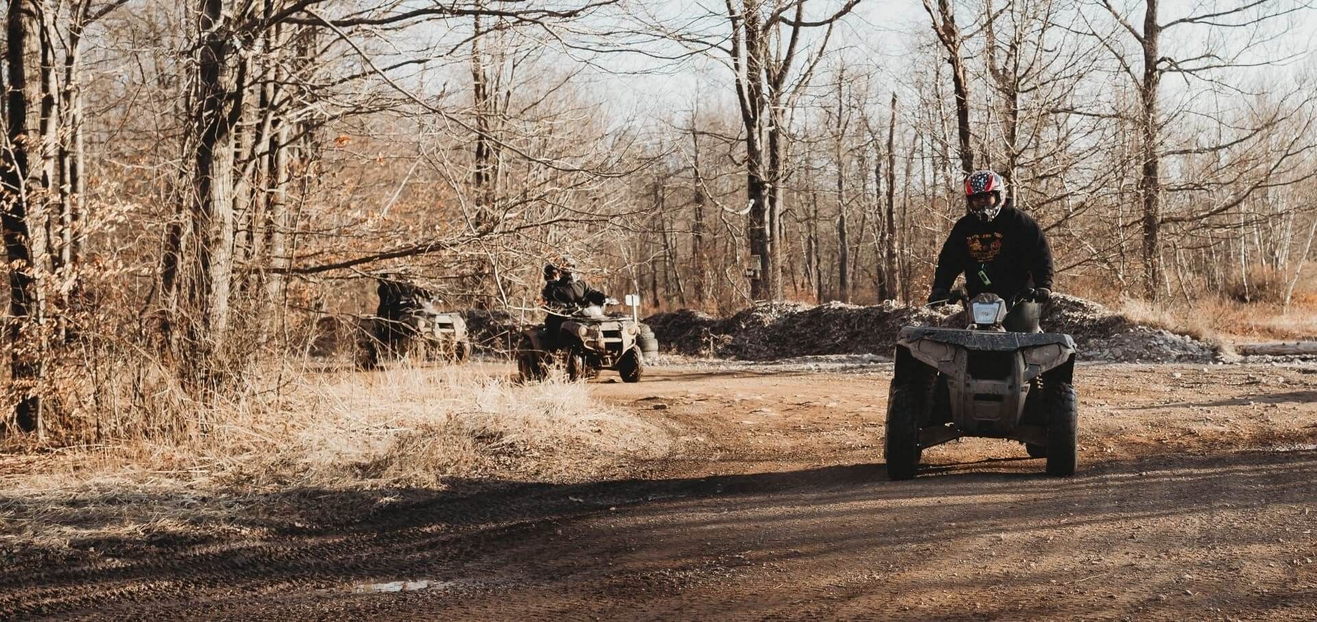 A man is riding an atv down a dirt road in the woods.