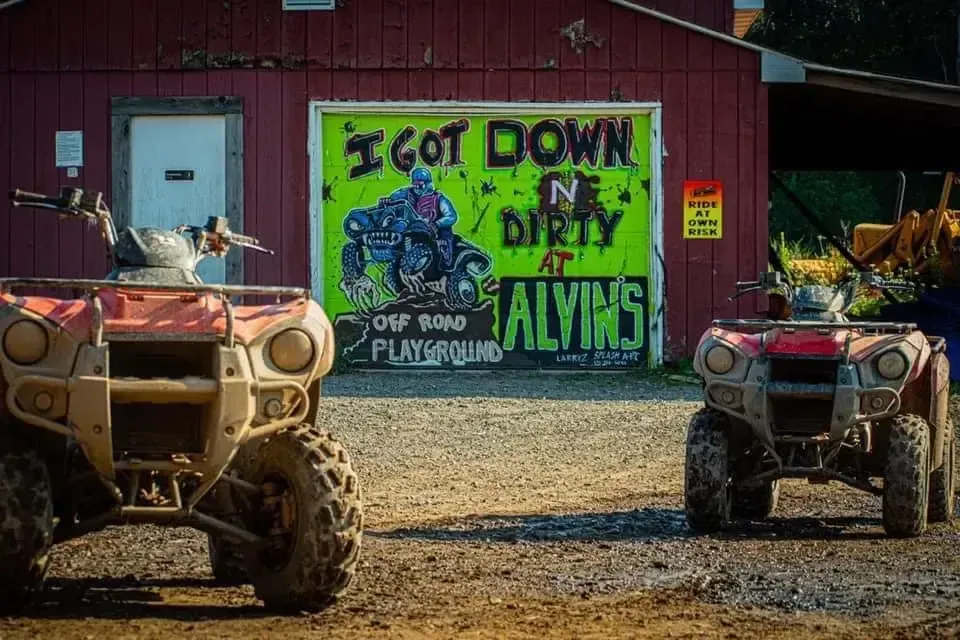 Two atvs are parked in front of a sign that says `` i got down no dirty alyins ''.