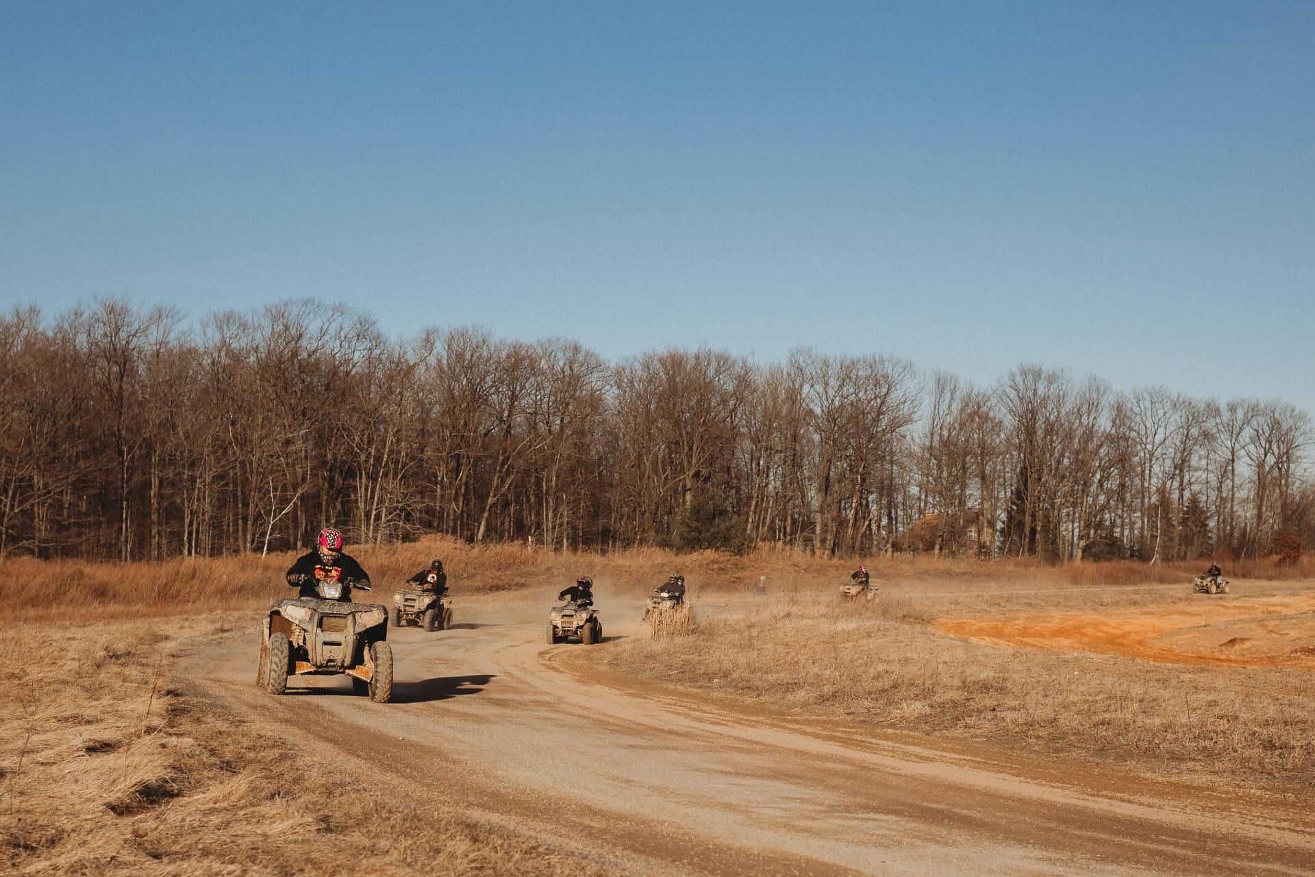 A group of people are riding atvs down a dirt road.