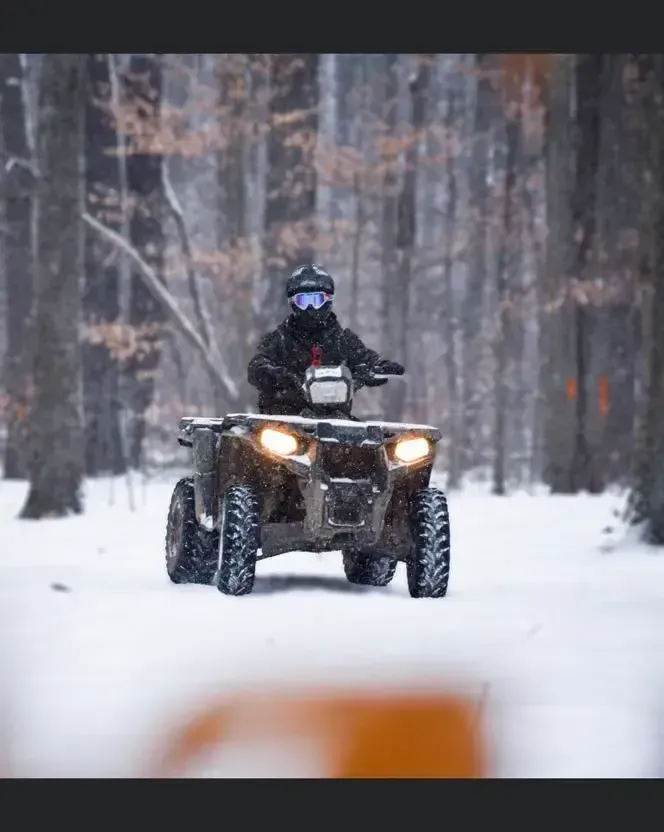 A man is riding an atv in the snow in the woods.