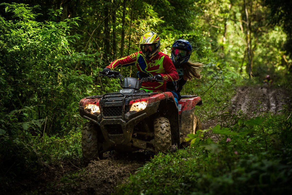 A man and a woman are riding an atv through the woods.