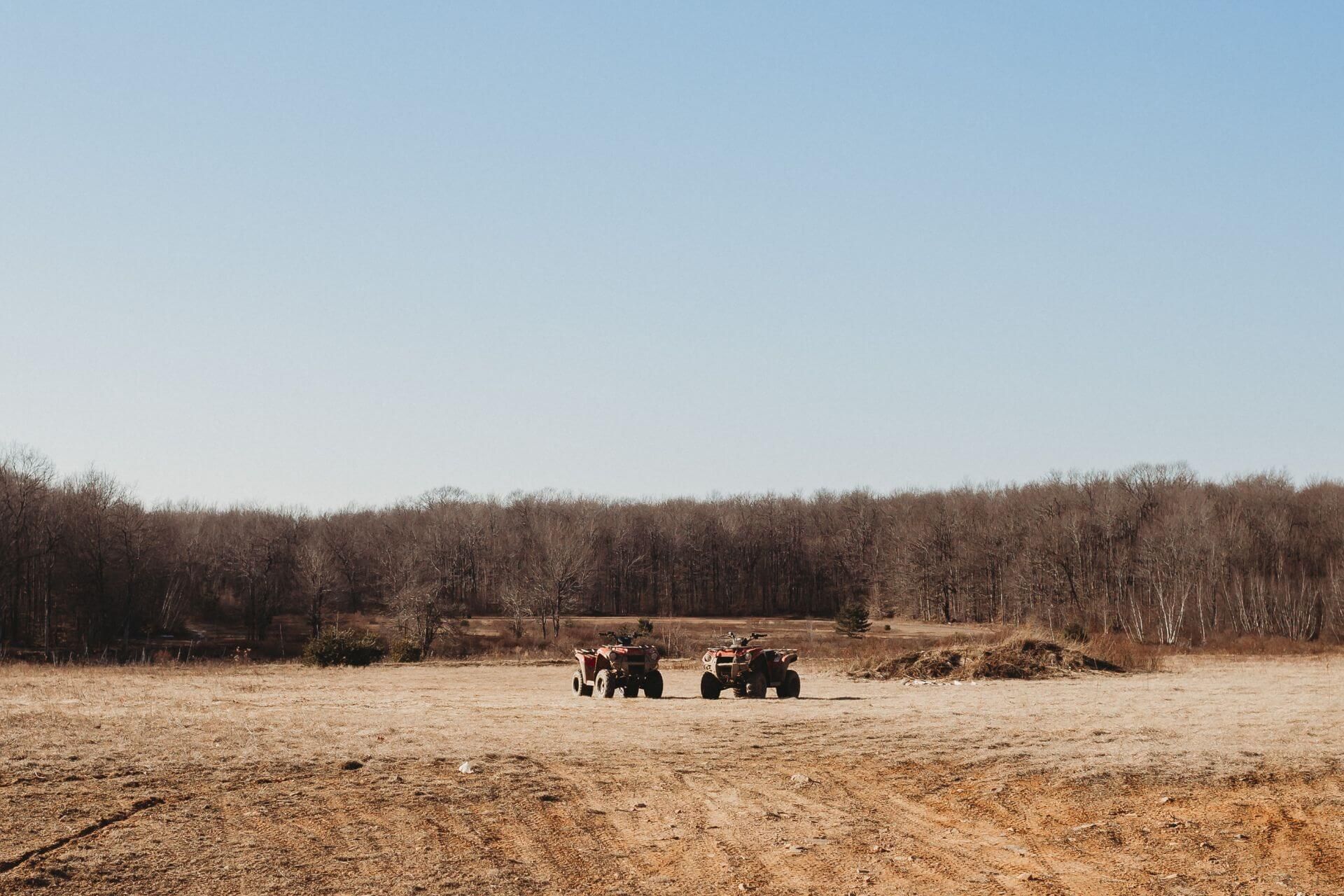 Two people are riding atvs in a field.