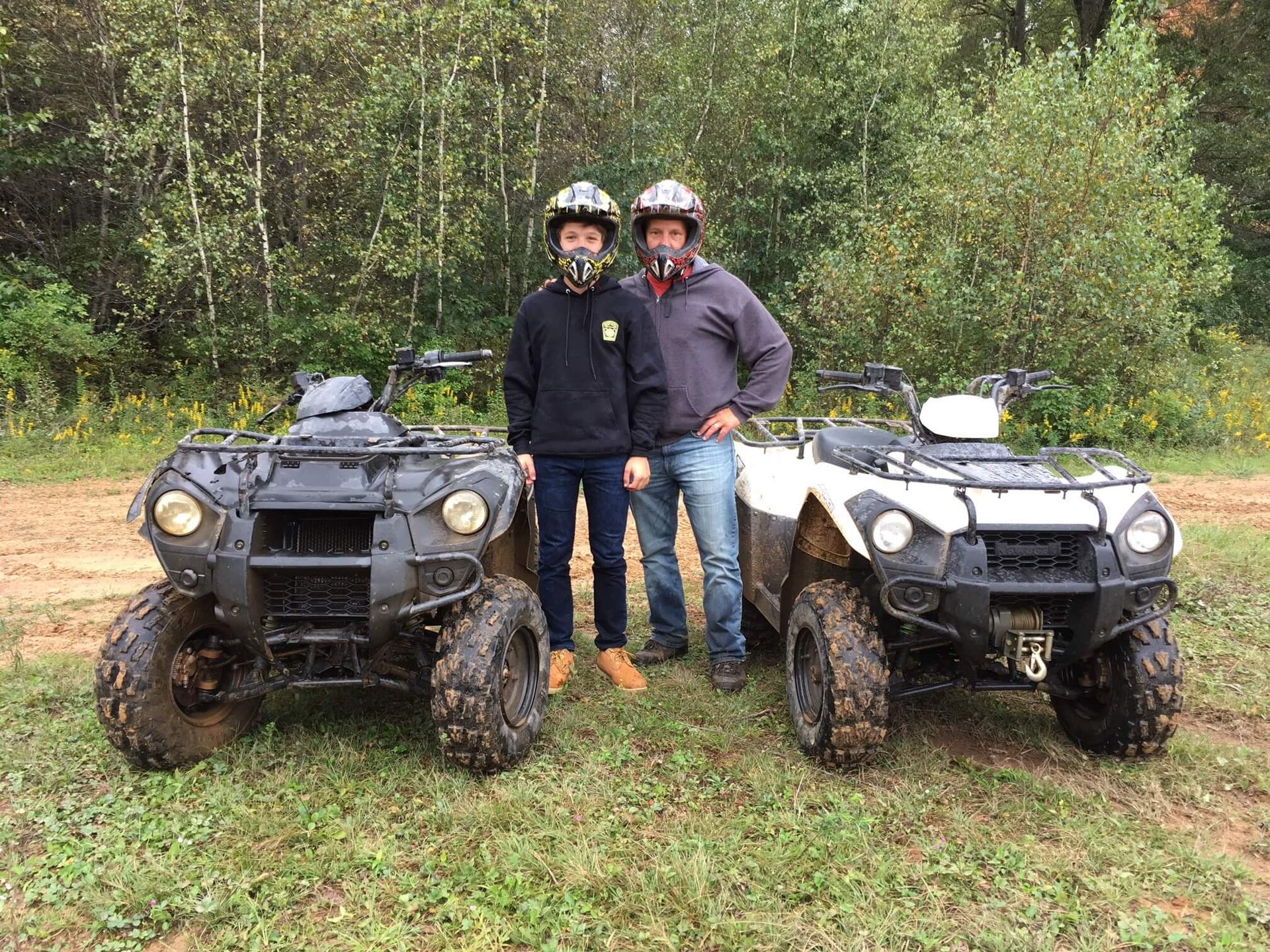 Two men are standing next to two atvs in a field.