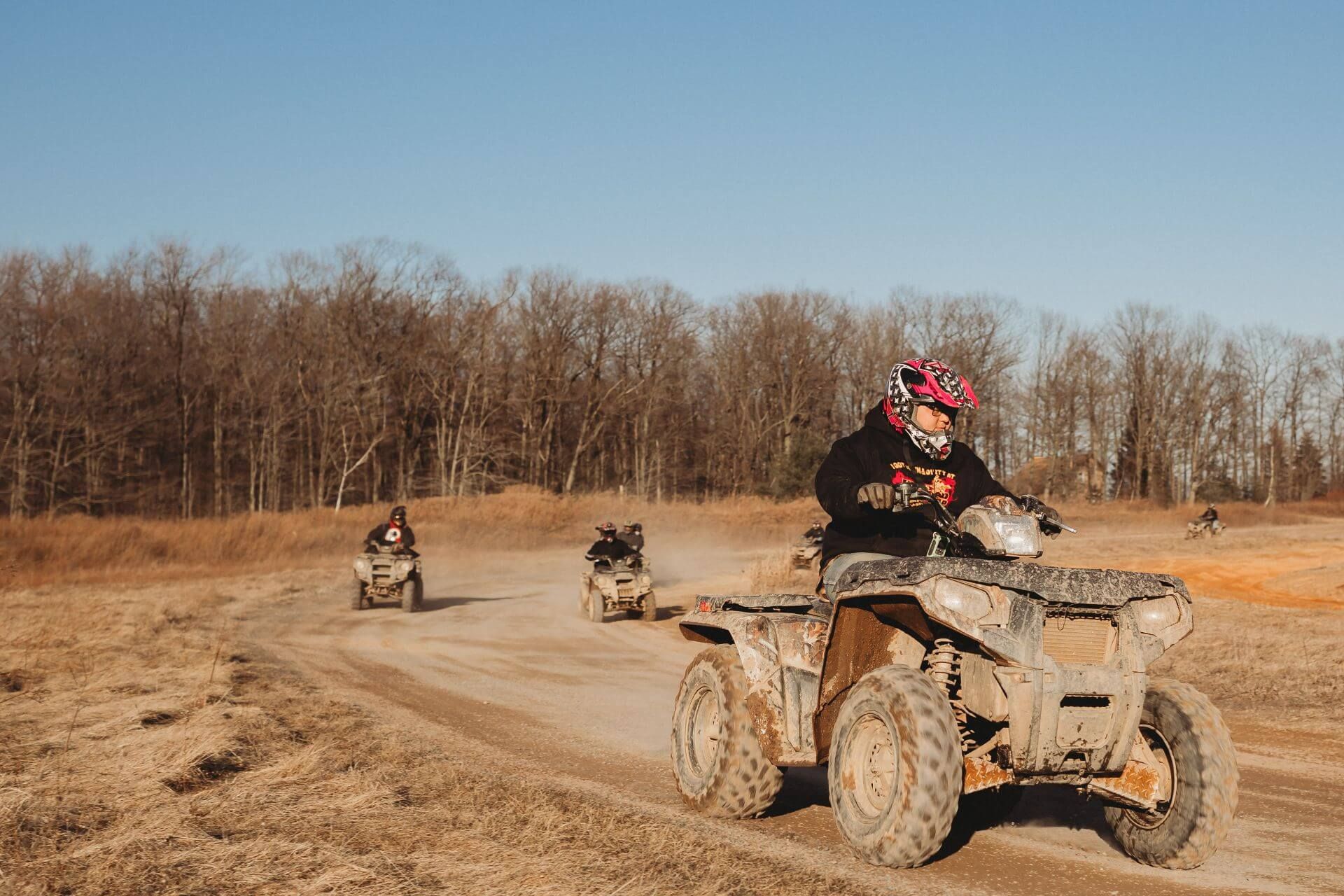 A group of people are riding atvs on a dirt road.
