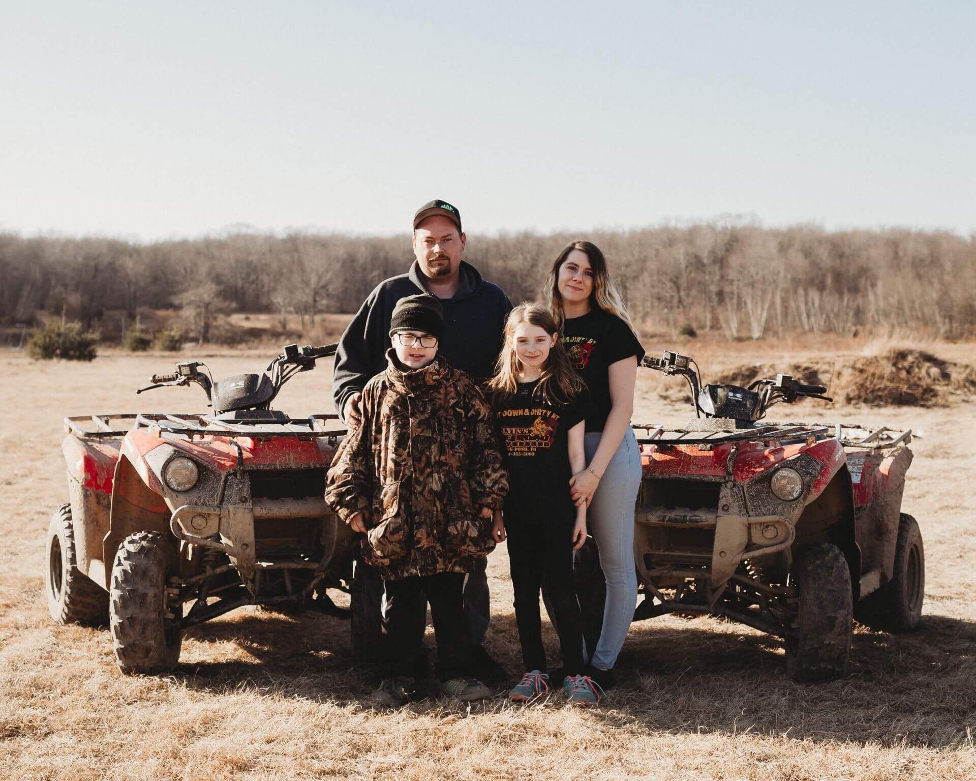 A family is posing for a picture in front of two atvs in a field.
