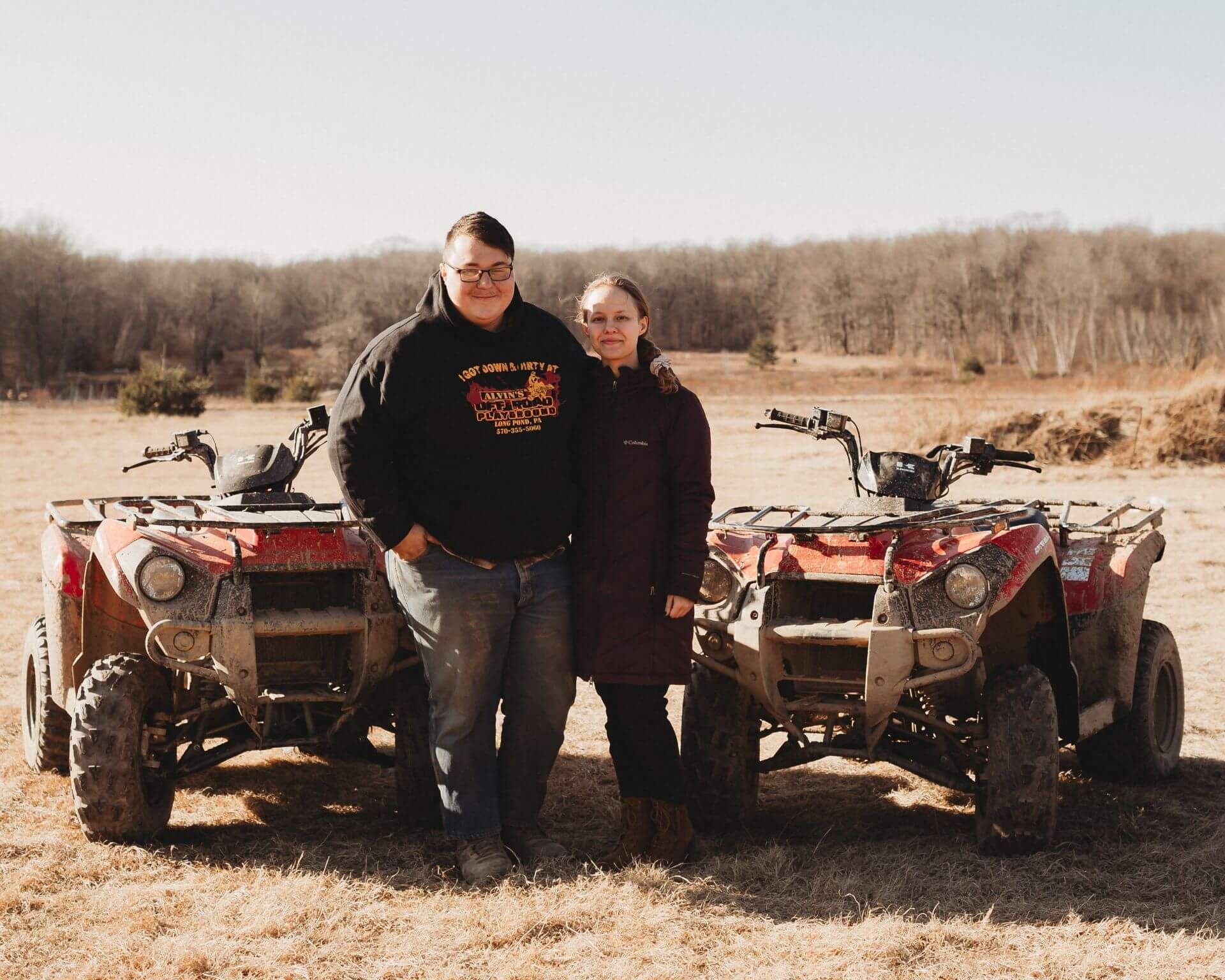 A man and a woman are standing in front of two atvs in a field.