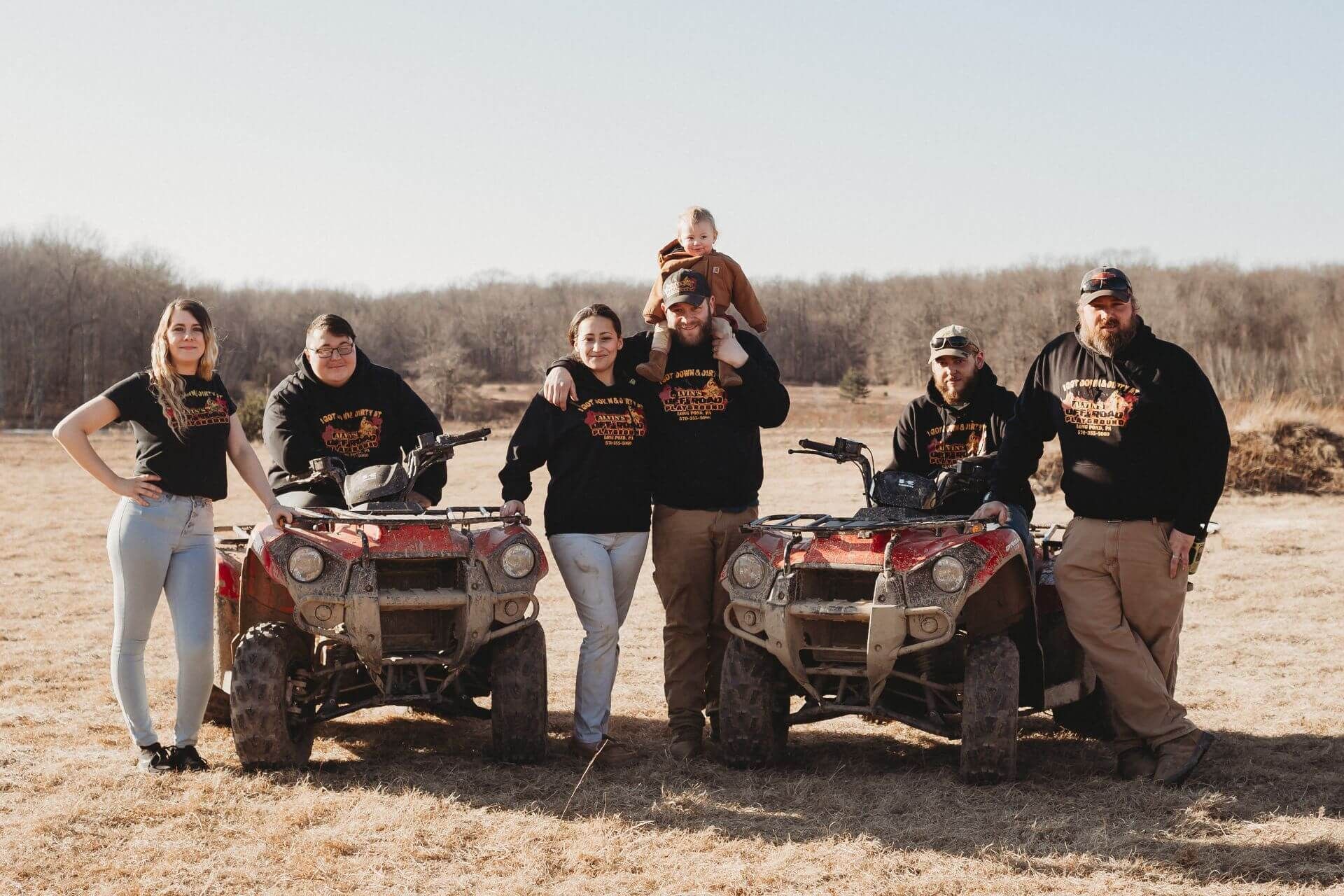 A group of people standing next to atvs in a field.