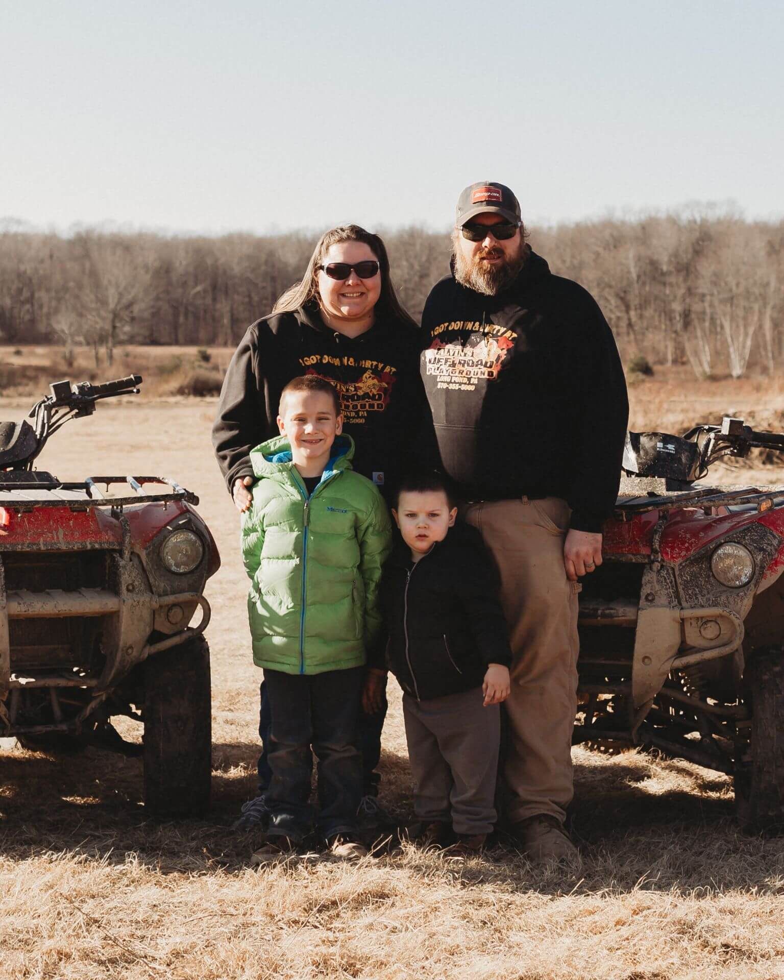 A family is posing for a picture in front of two atvs.