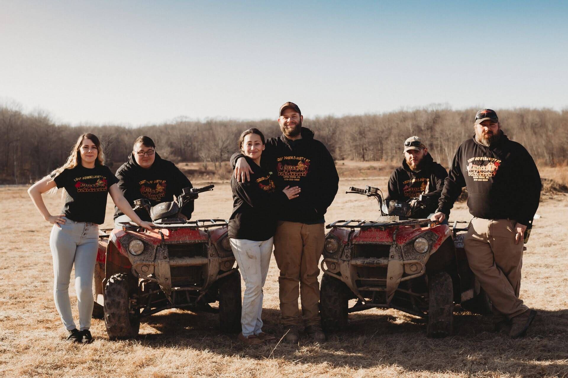 A group of people standing next to four wheelers in a field.