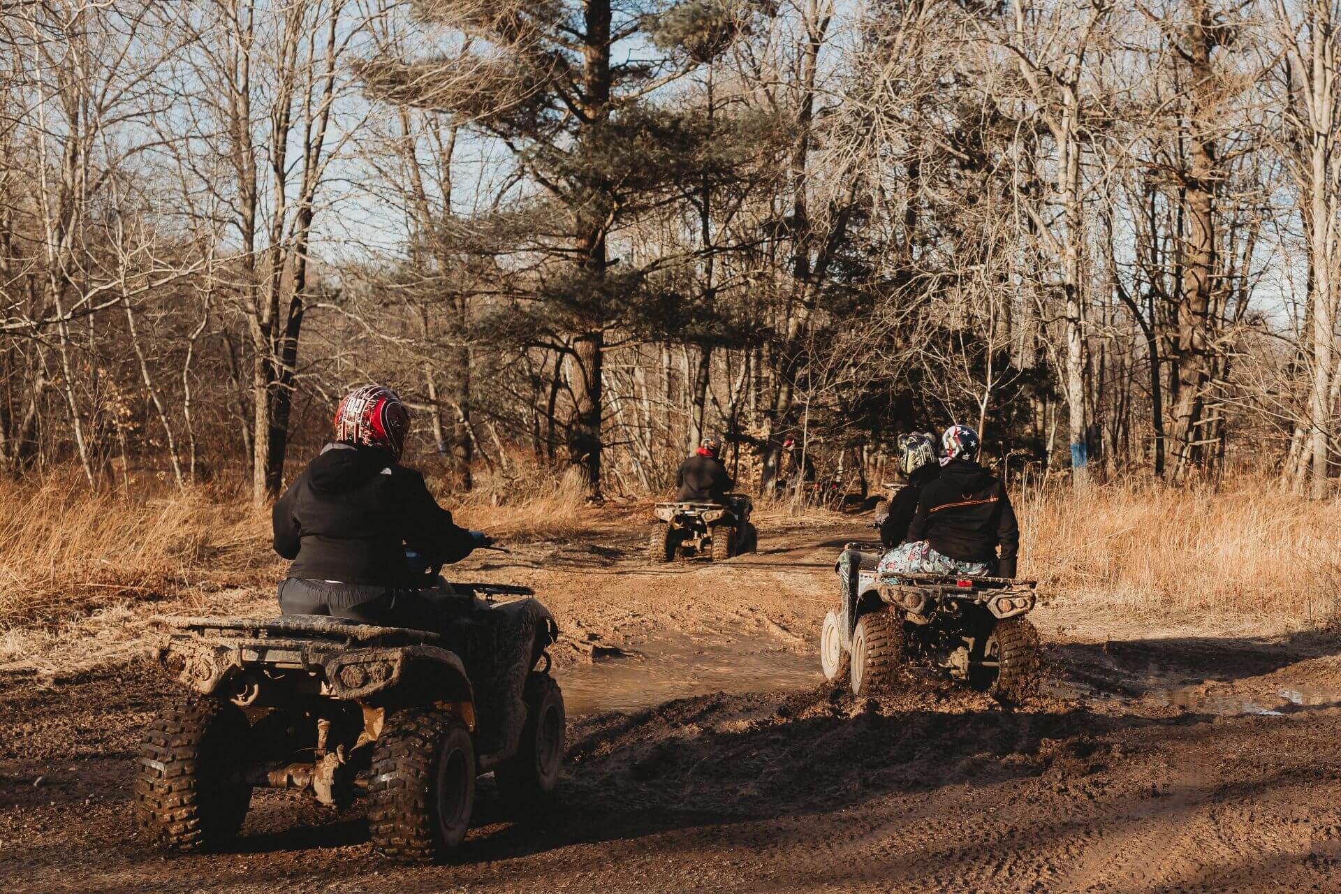 A group of people are riding atvs on a dirt road in the woods.