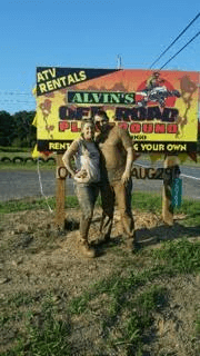 A man and a woman are standing in front of a sign for alvin 's off road playground.