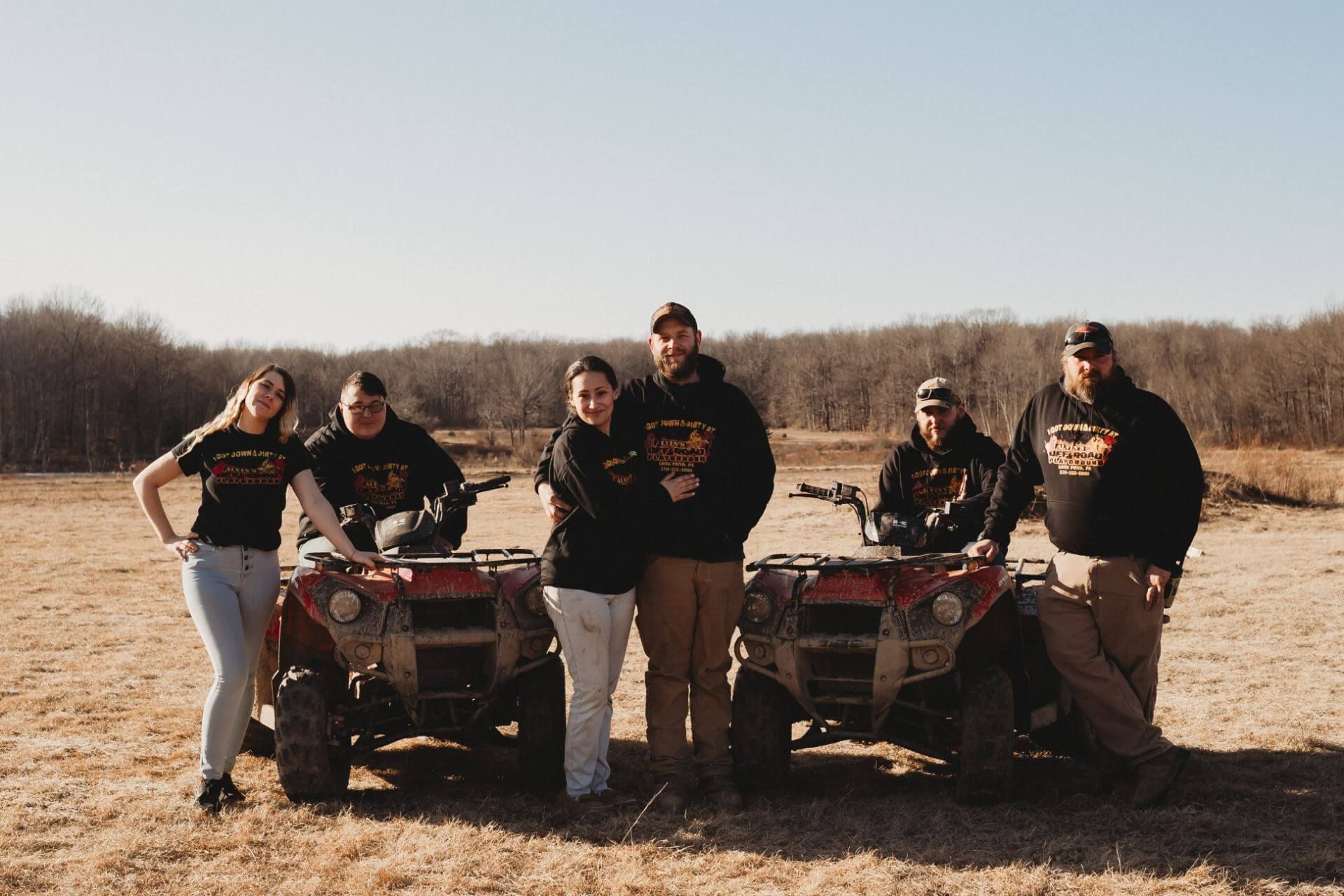 A group of people standing next to atvs in a field.