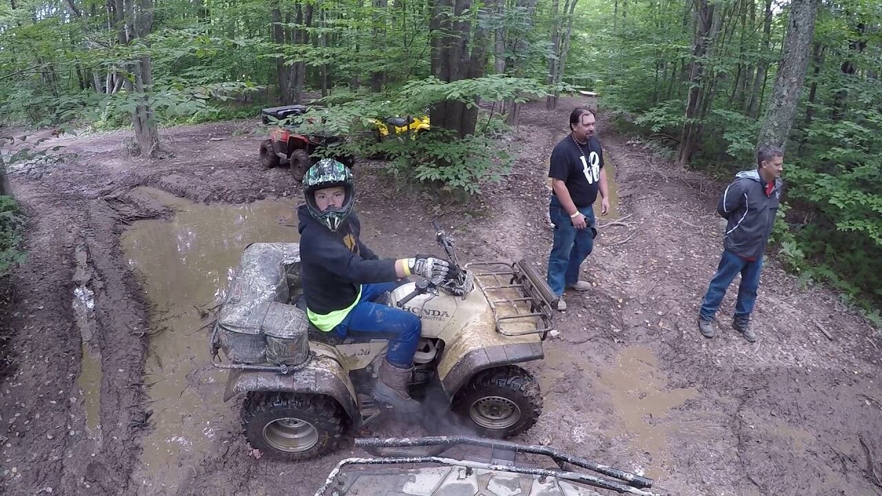 A man is riding a four wheeler through the mud in the woods.