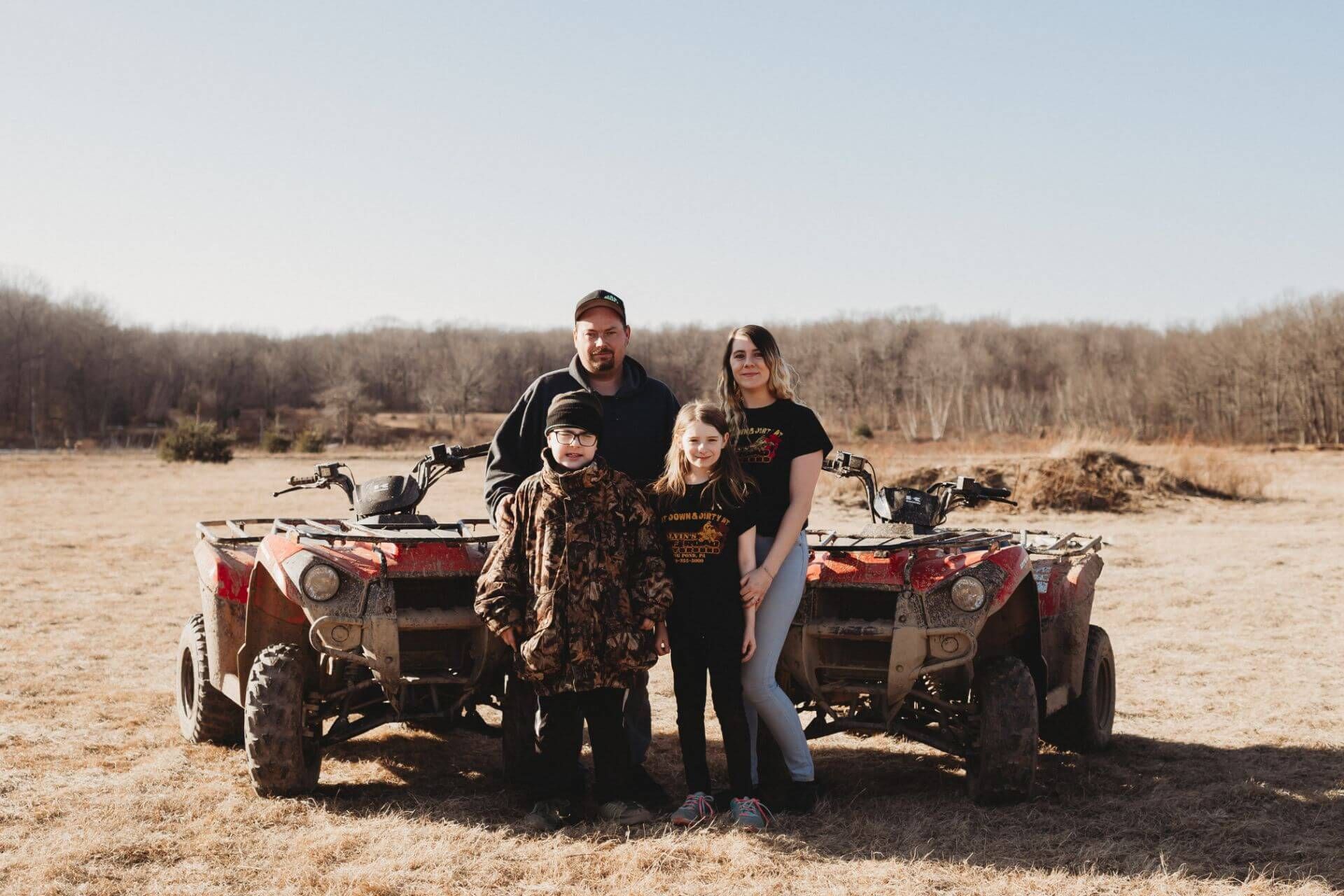A family is standing in front of two atvs in a field.