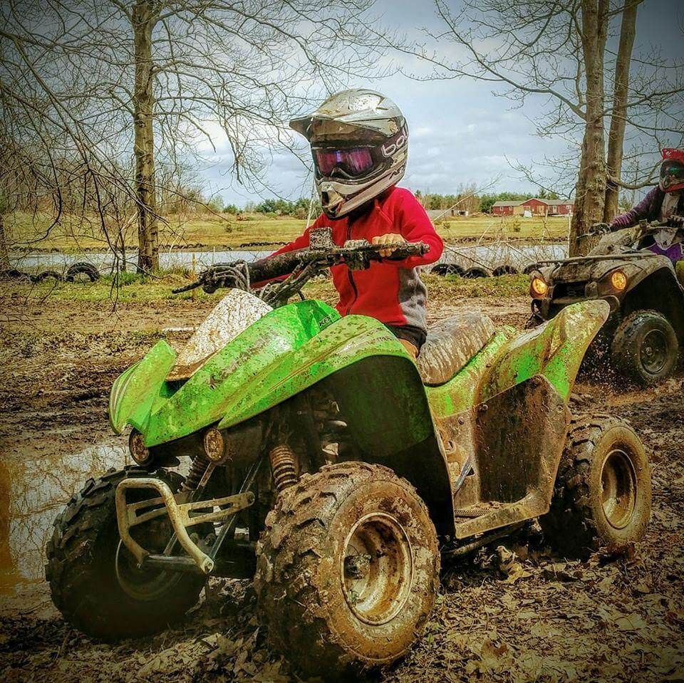 A person is riding a green atv in the mud.