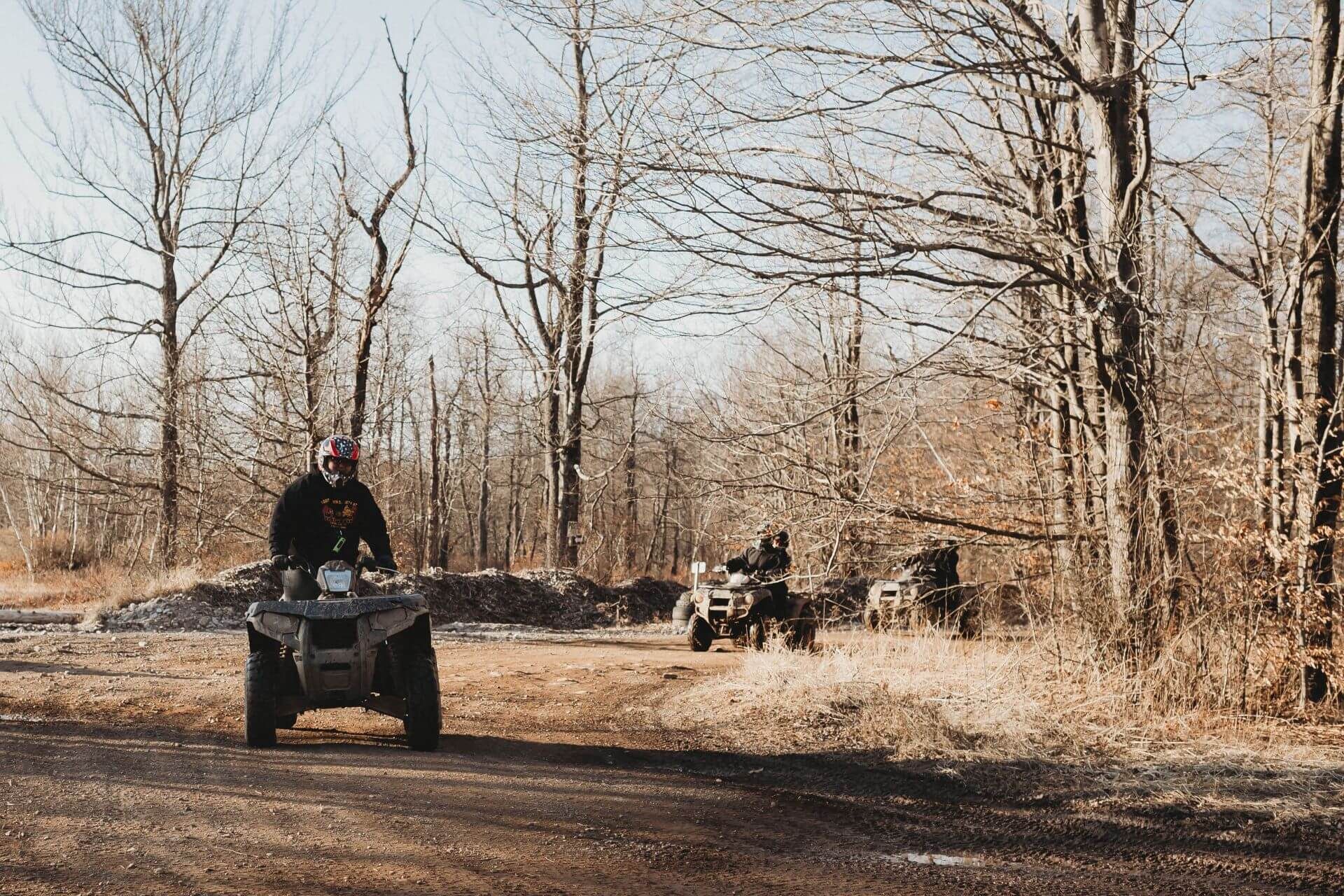 A man is riding an atv down a dirt road in the woods.