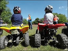 Two young boys are riding atvs in a field.