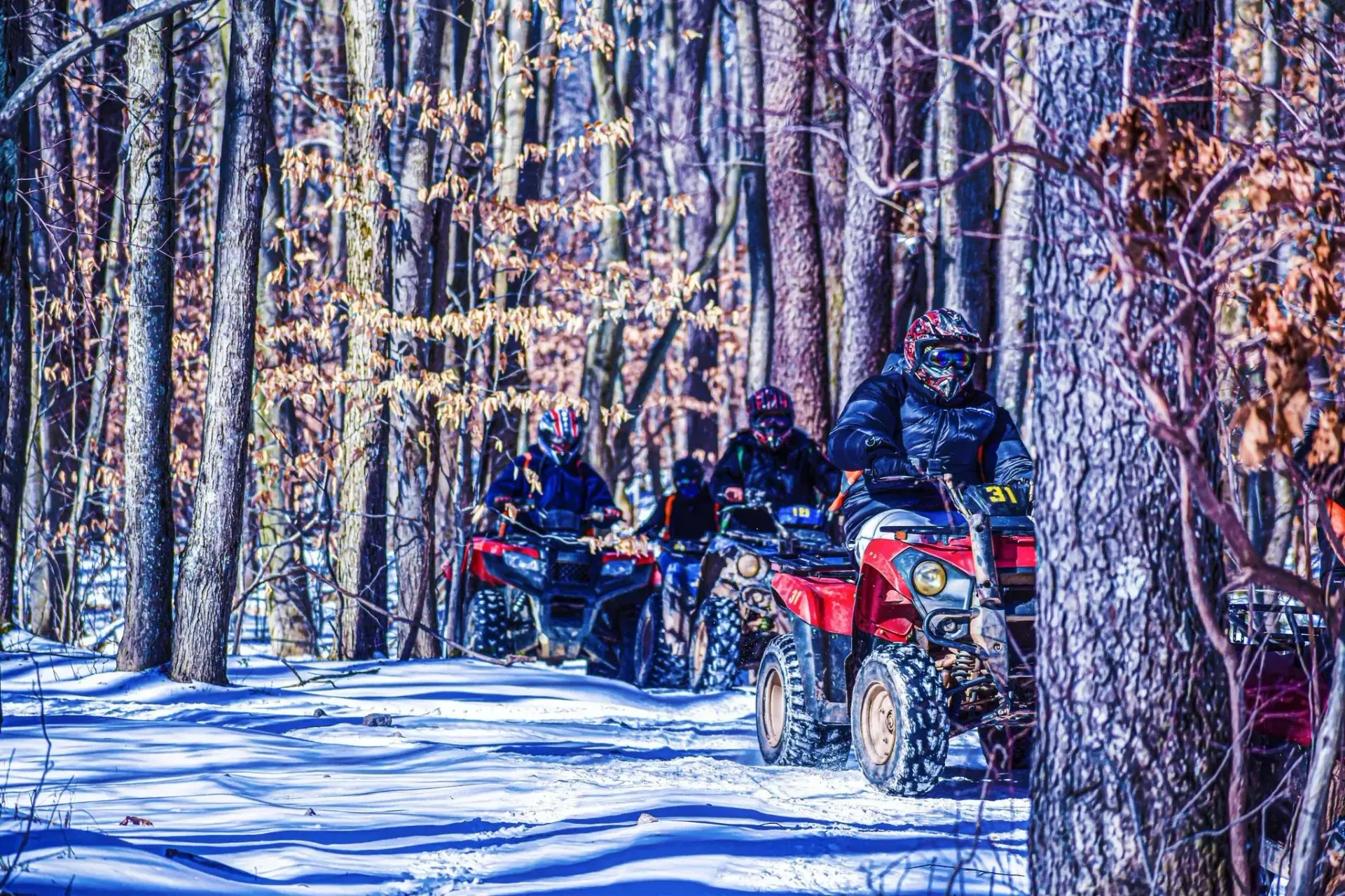 A group of people are riding atvs down a snowy trail in the woods.