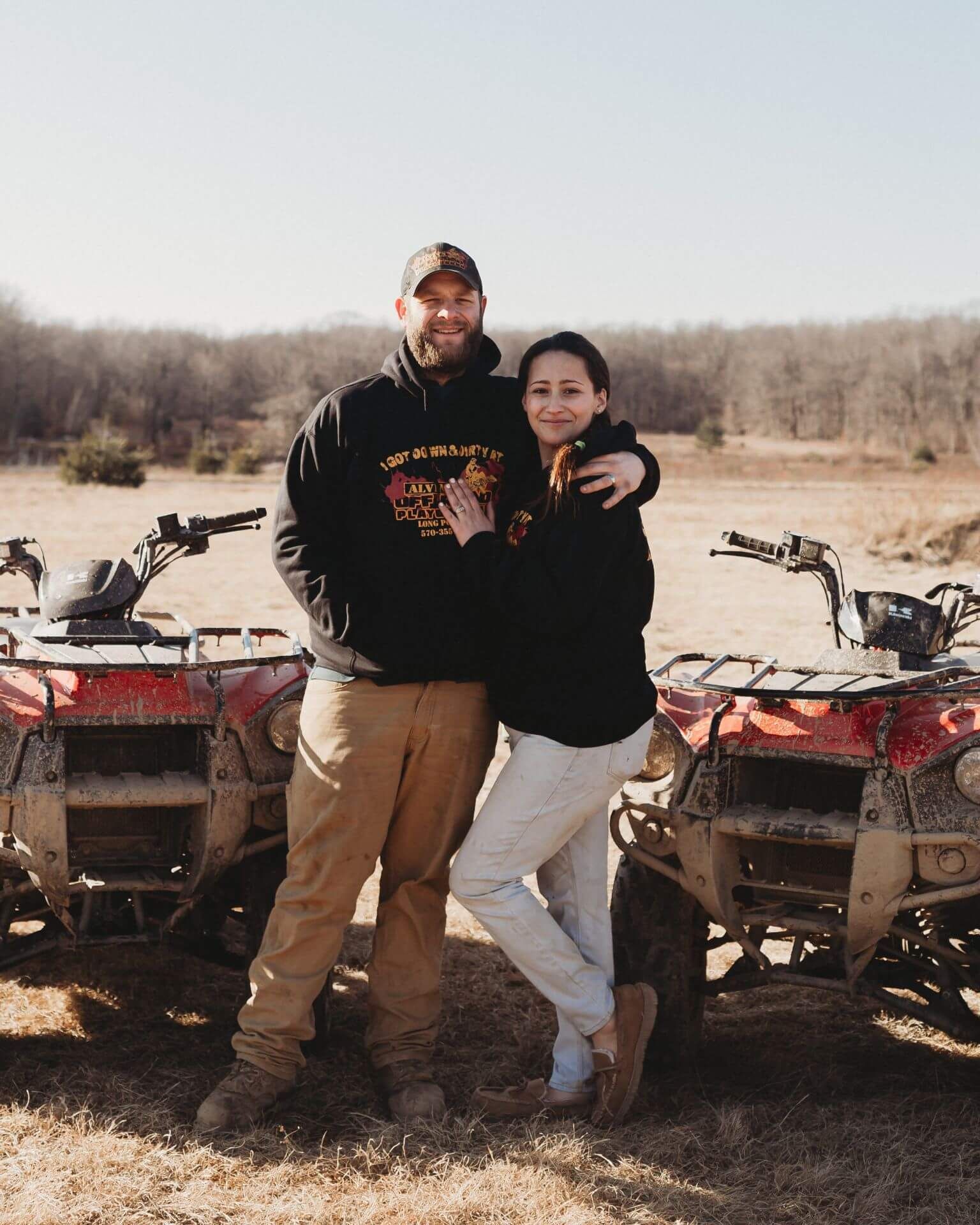 A man and a woman are standing next to atvs in a field.