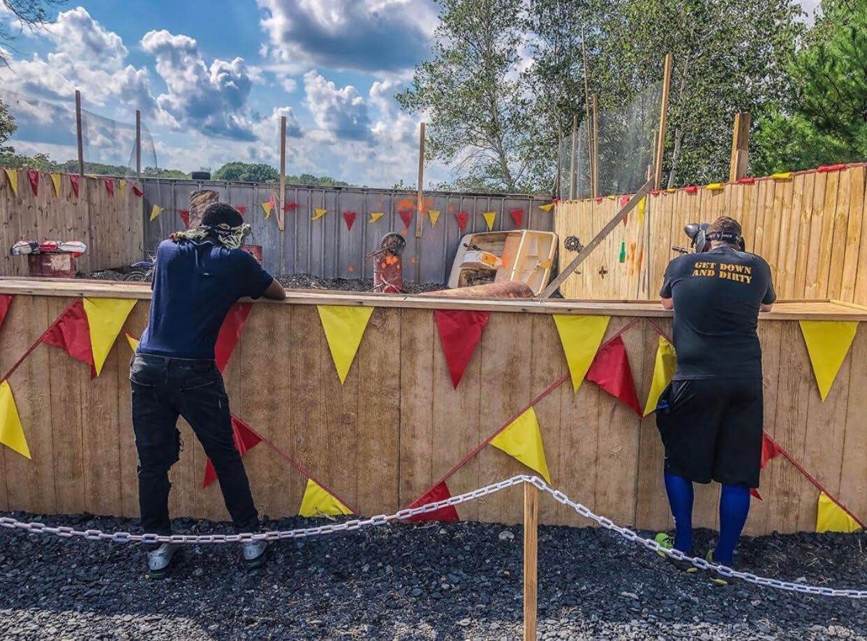 Two men are standing in front of a wooden fence with yellow and red flags.