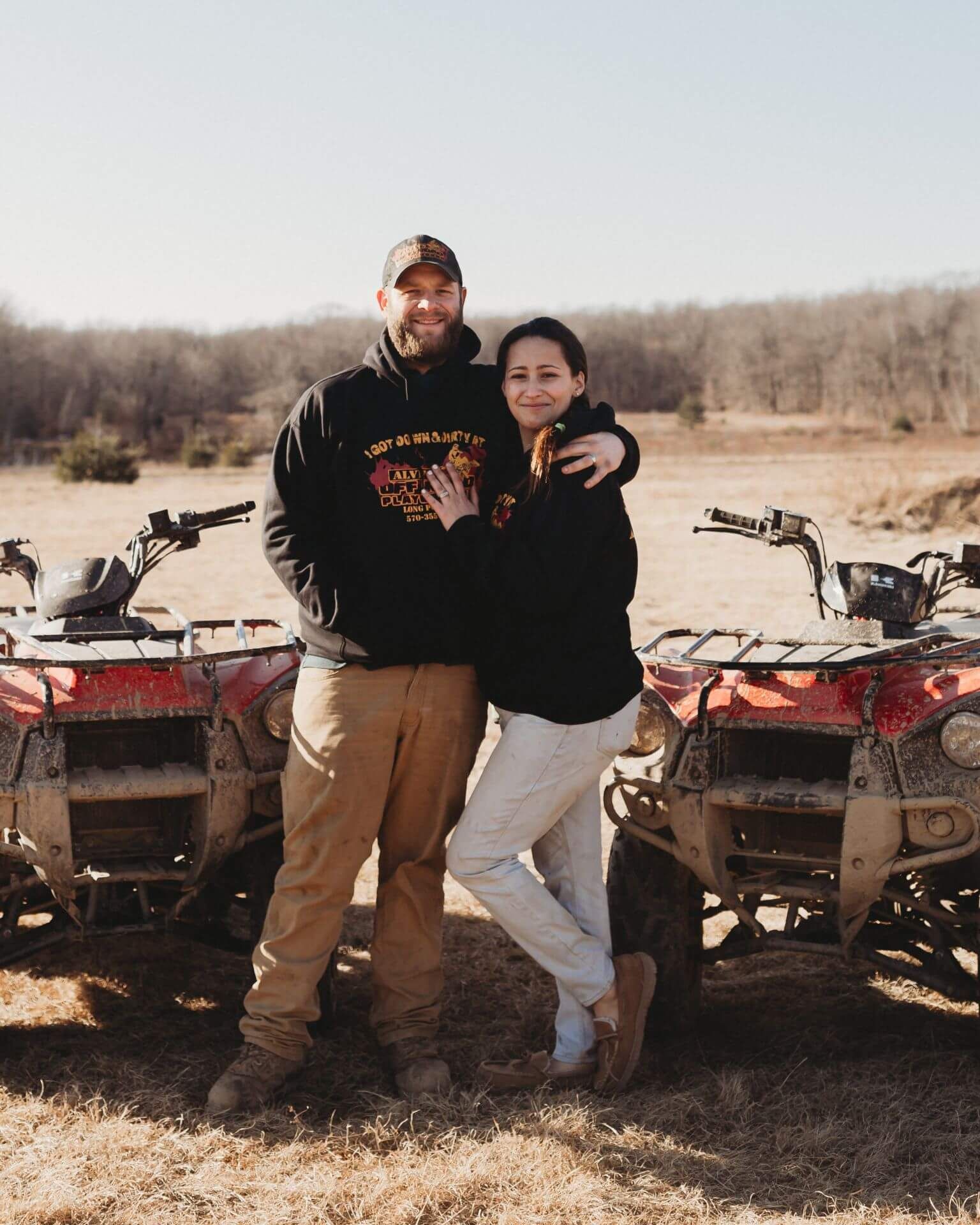 A man and a woman are standing next to two atvs in a field.