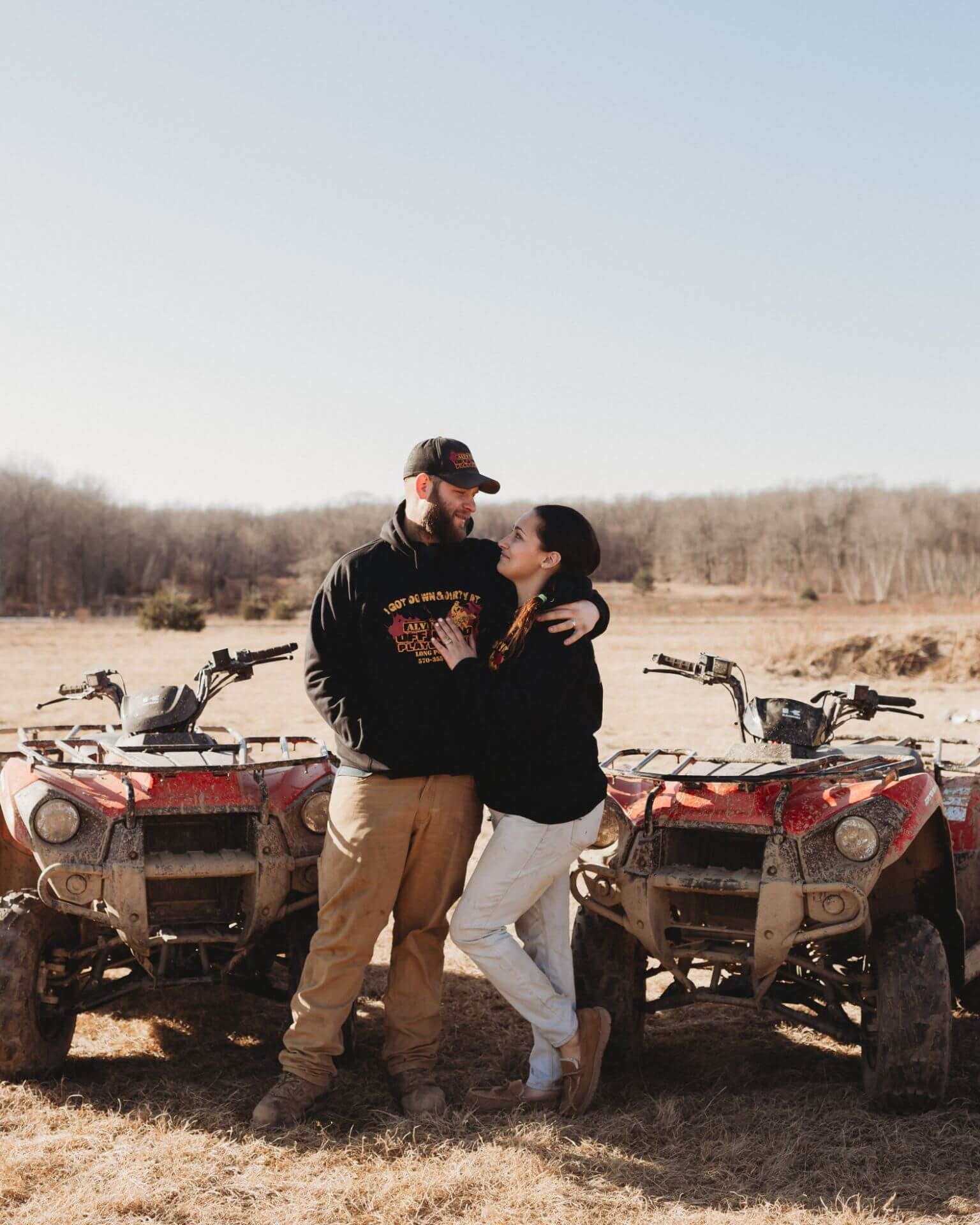 A man and a woman are standing next to atvs in a field.
