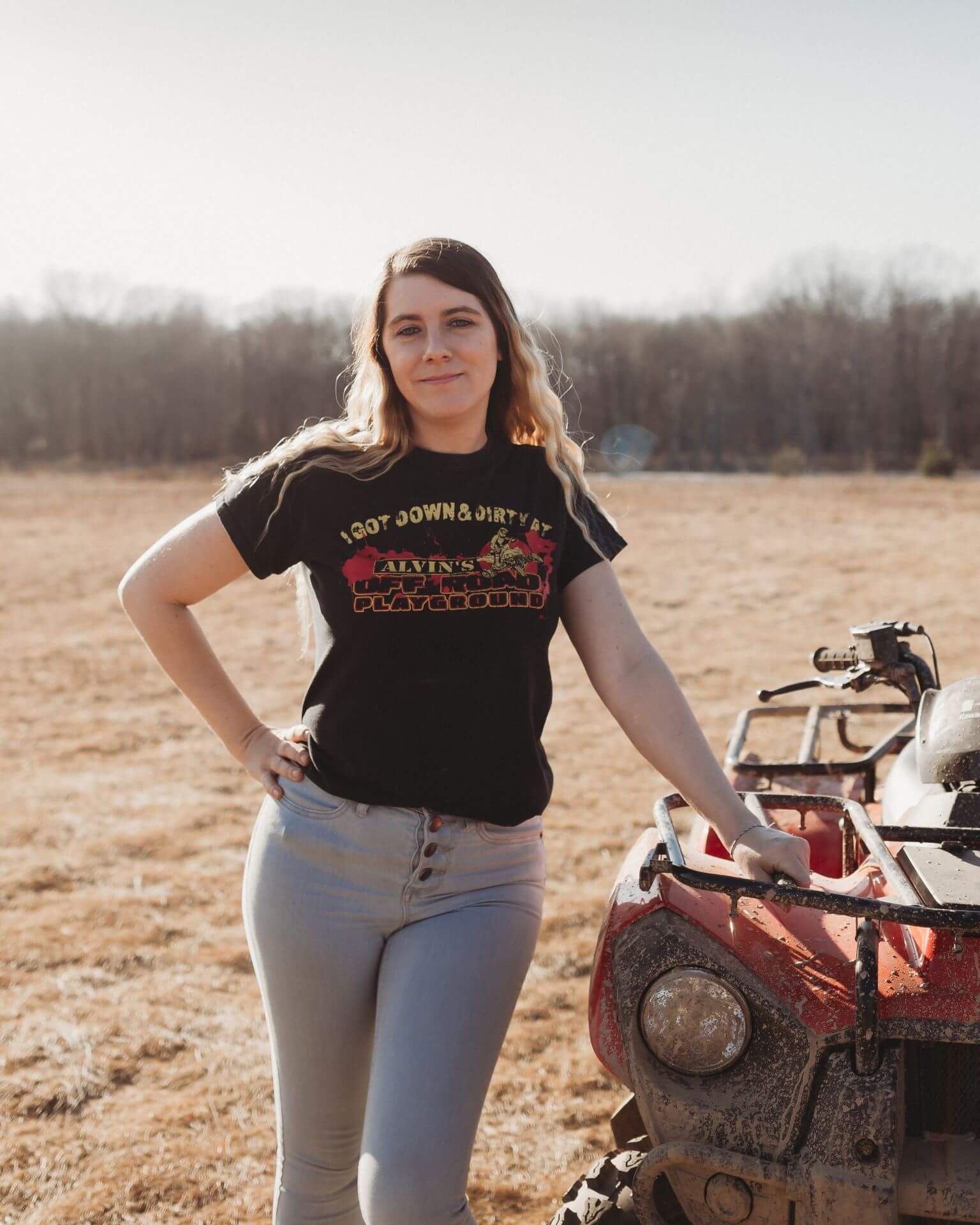 A woman is standing next to a red atv in a field.