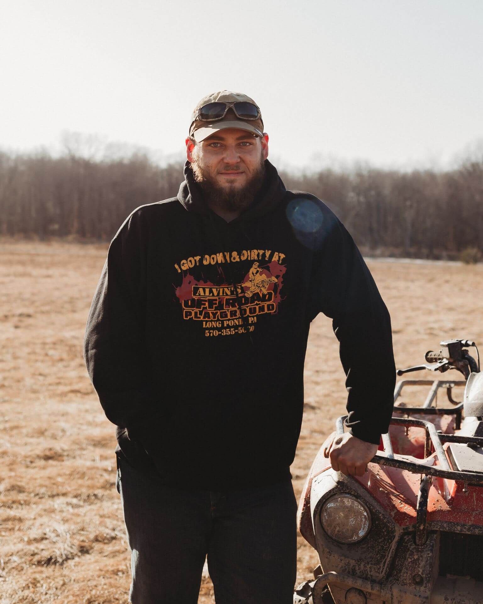 A man in a black hoodie is standing next to a red atv in a field.