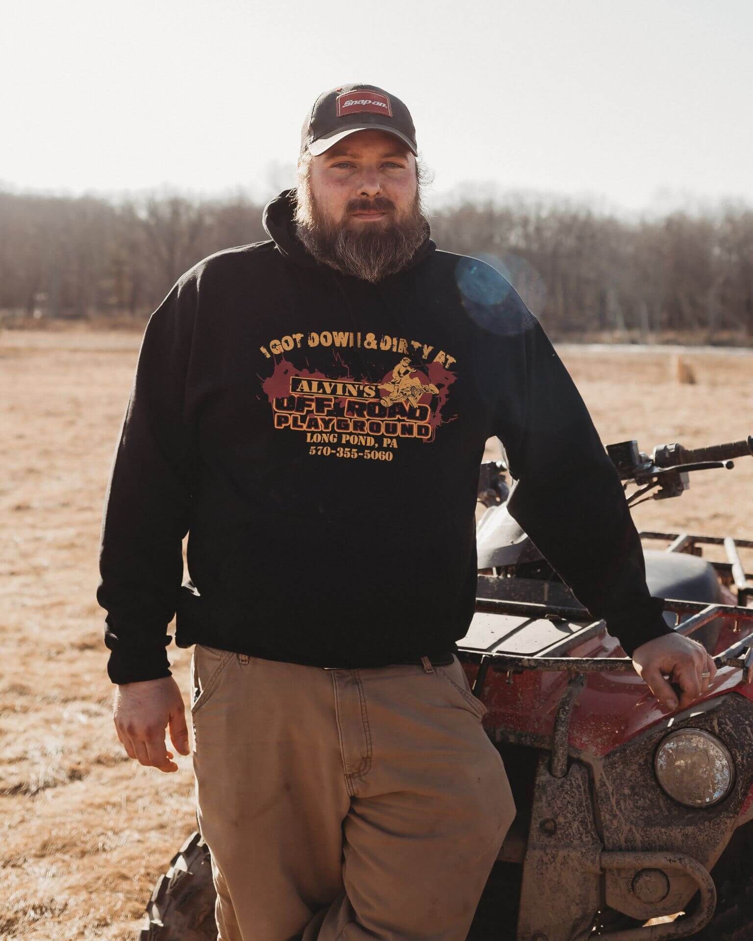 A man in a black hoodie is standing next to a red atv